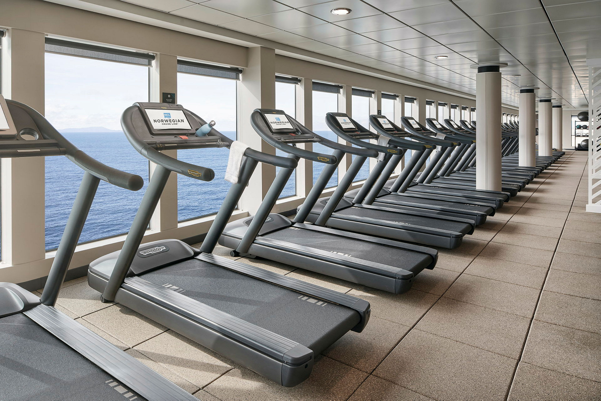 En rekke tredemøller på et treningsstudio med utsikt over havet. (AI-generert tekst)