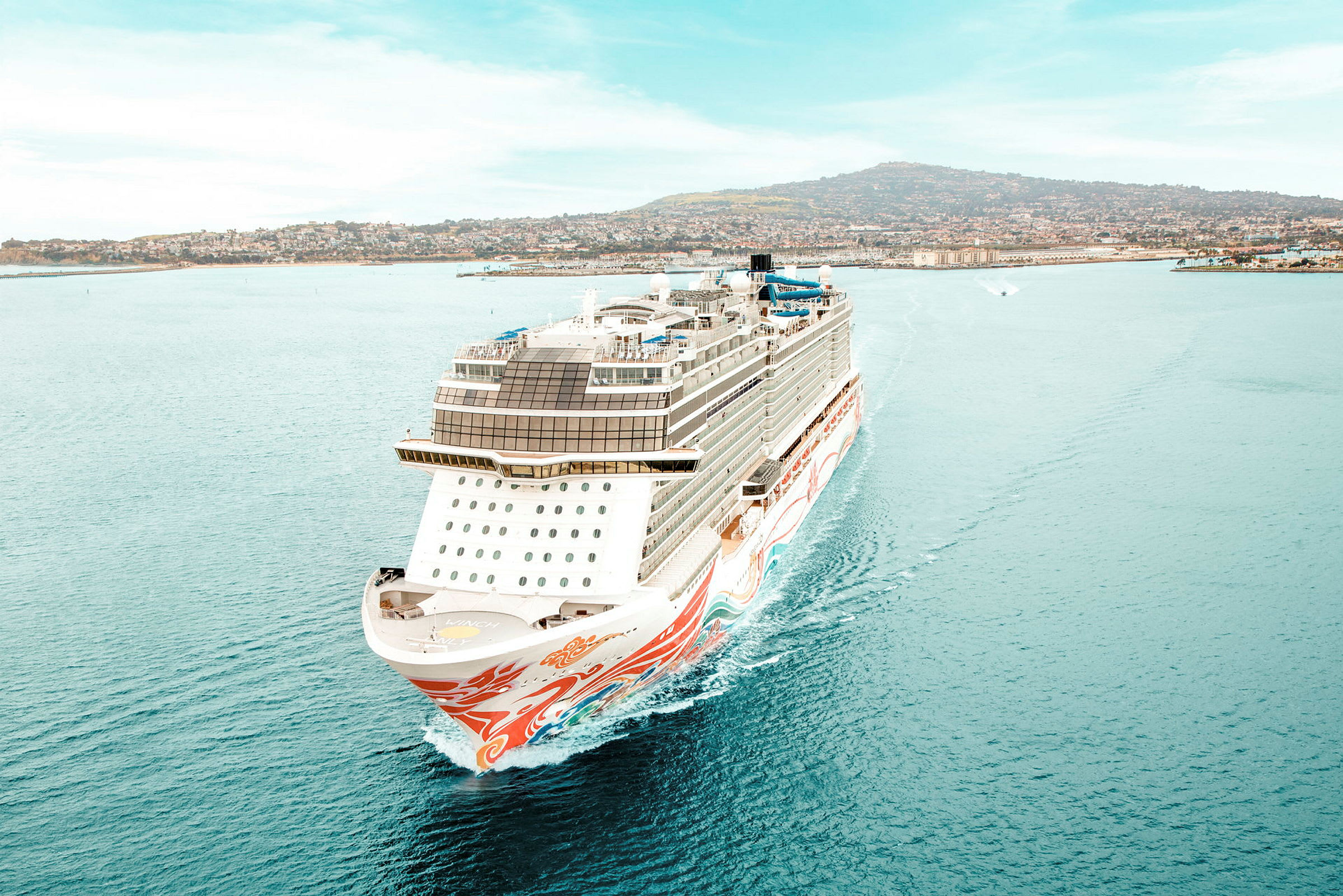 Et cruiseskip på havet med en by og en fjellkyst i bakgrunnen. (AI-generert tekst)