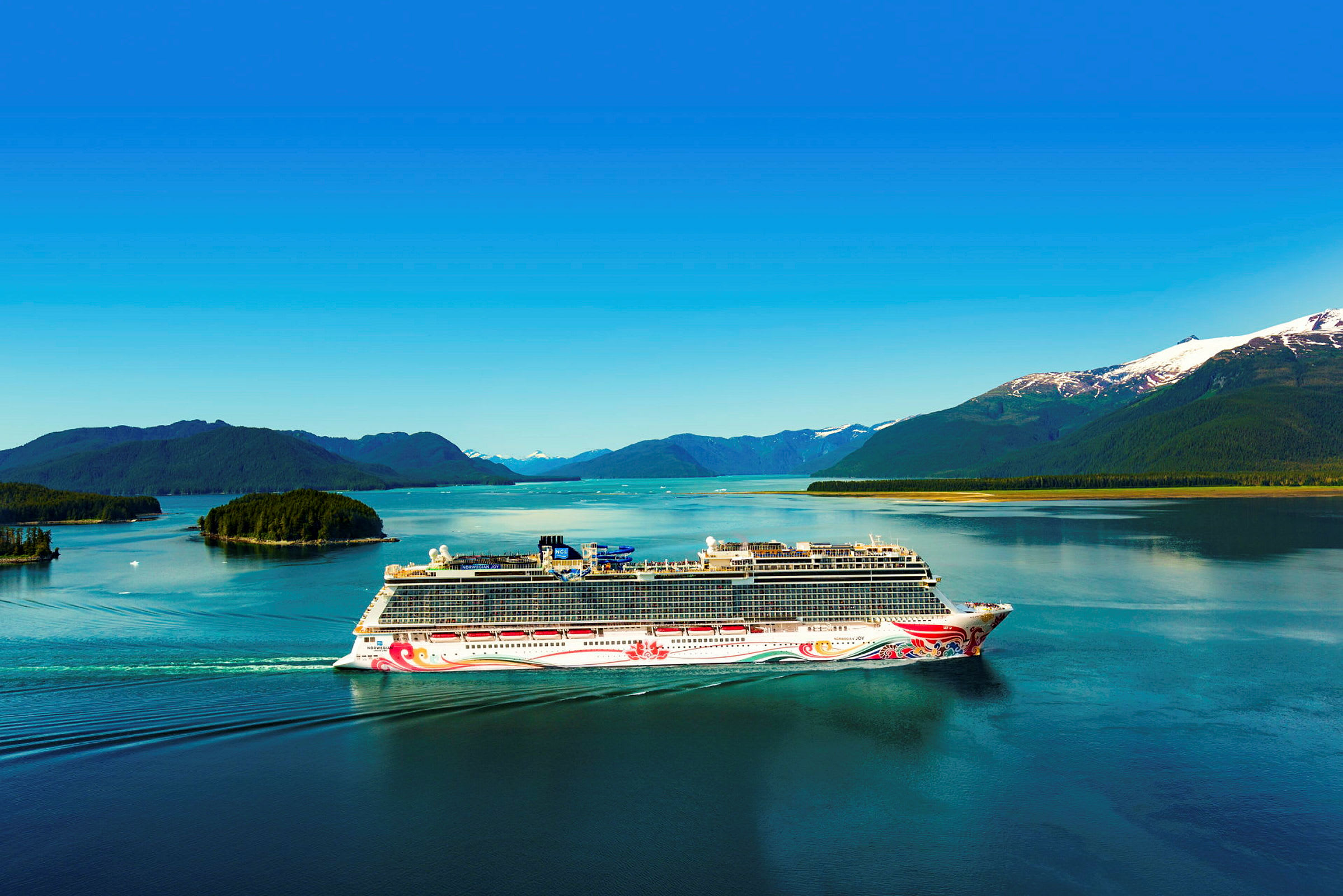 Et cruiseskip seiler på en klar innsjø omgitt av skogkledde fjell og små øyer. (AI-generert tekst)