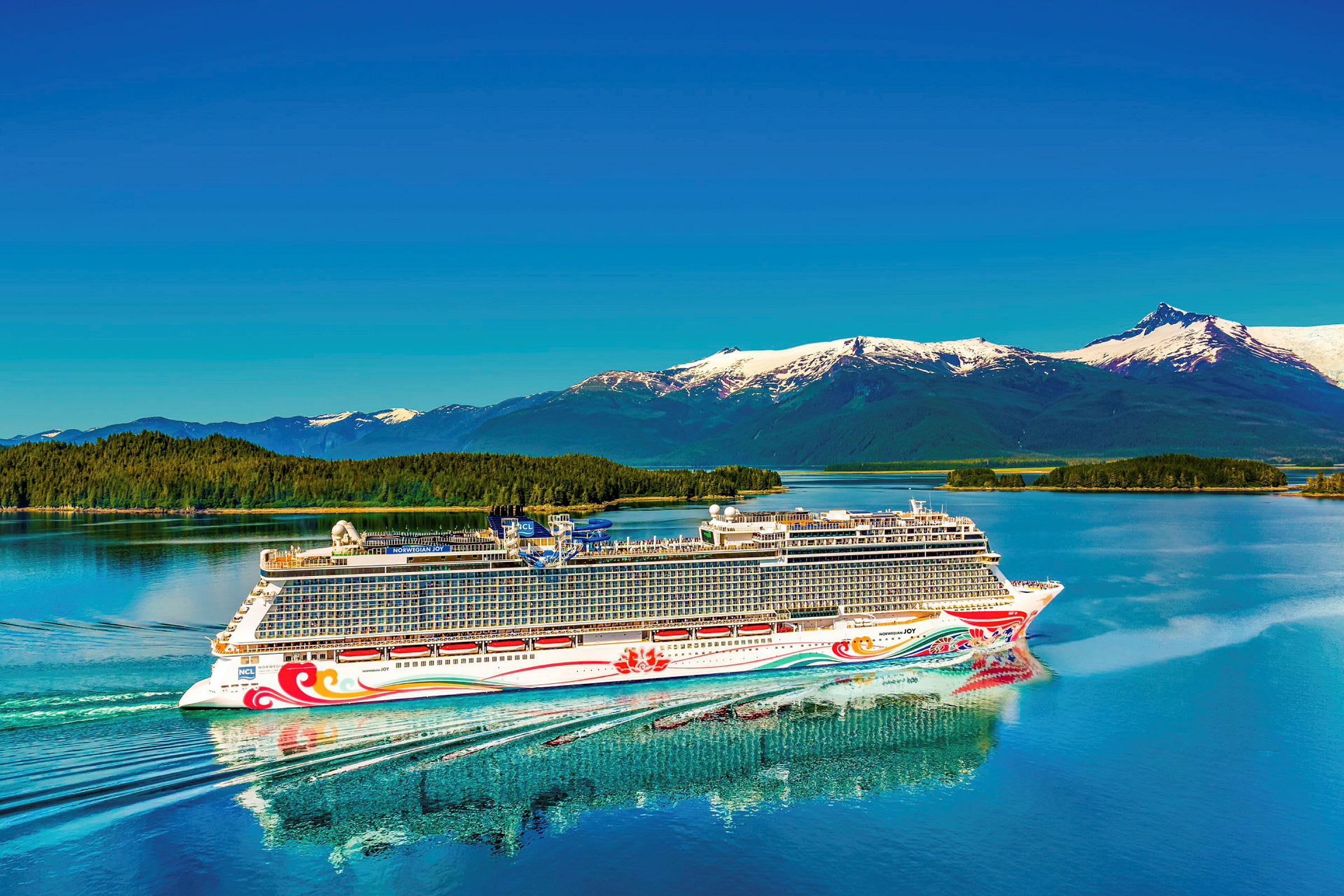 Et cruiseskip seiler på en rolig innsjø med snødekte fjell i bakgrunnen. (AI-generert tekst)