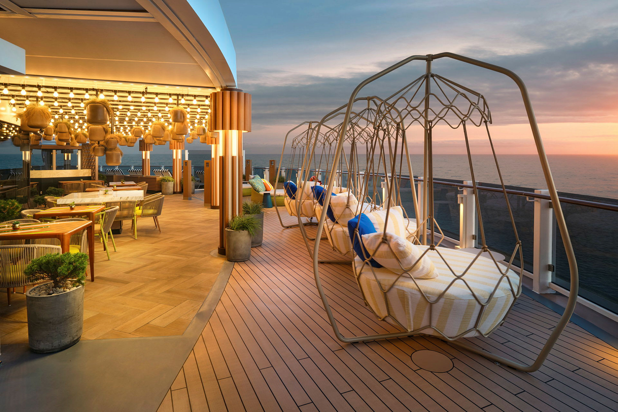 En takterrasse med hengende stoler og utsikt over havet ved solnedgang. (AI-generert tekst)
