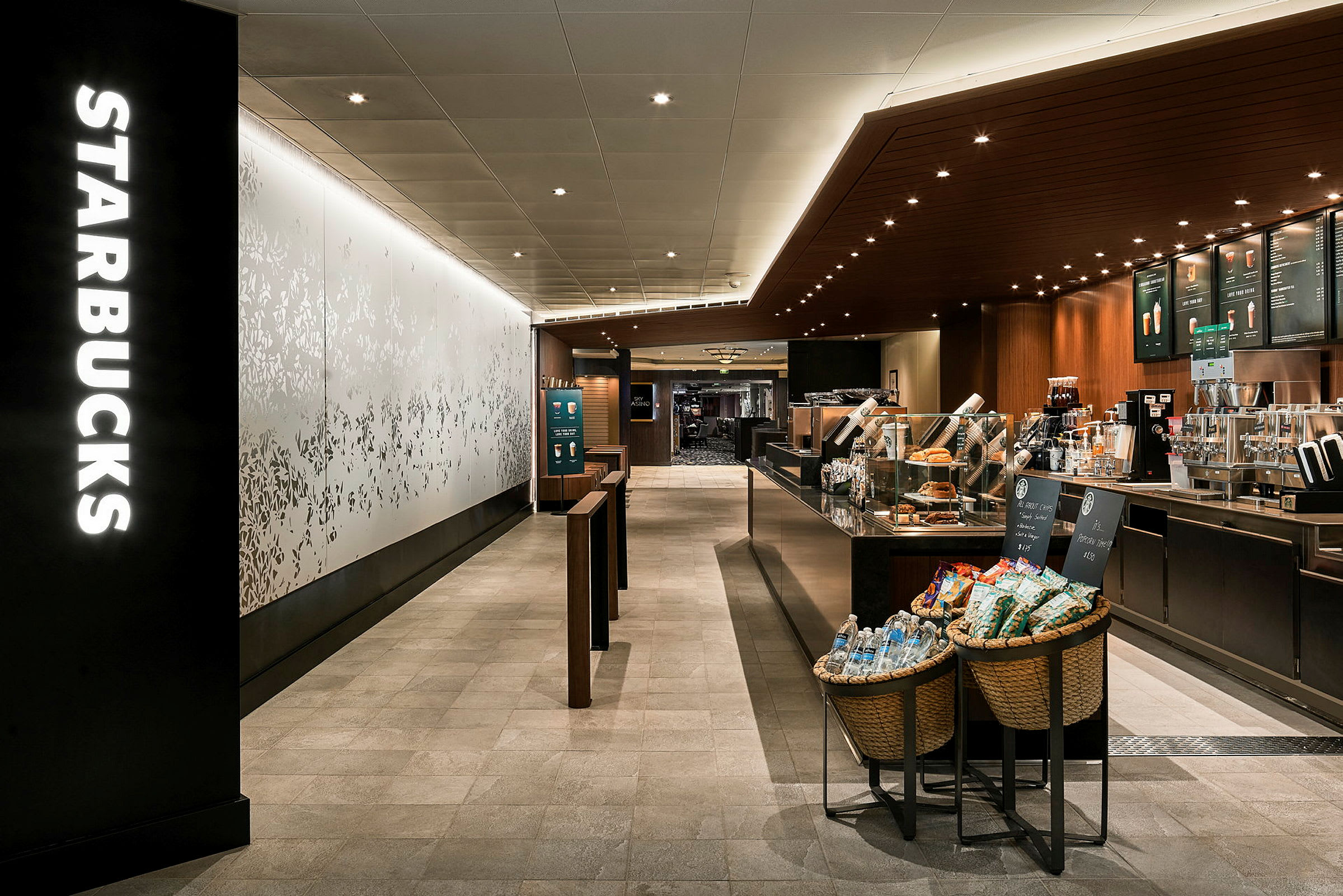 Et interiørbilde av en Starbucks-kafé med kaffemaskiner, menybrett og varer ved inngangen. (AI-generert tekst)