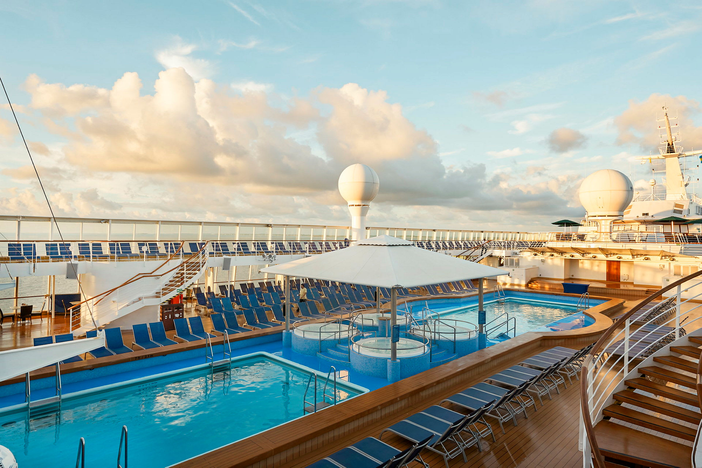 Bilde av et cruiseskip med to bassenger og mange solsenger på dekket under en blå himmel. (AI-generert tekst)