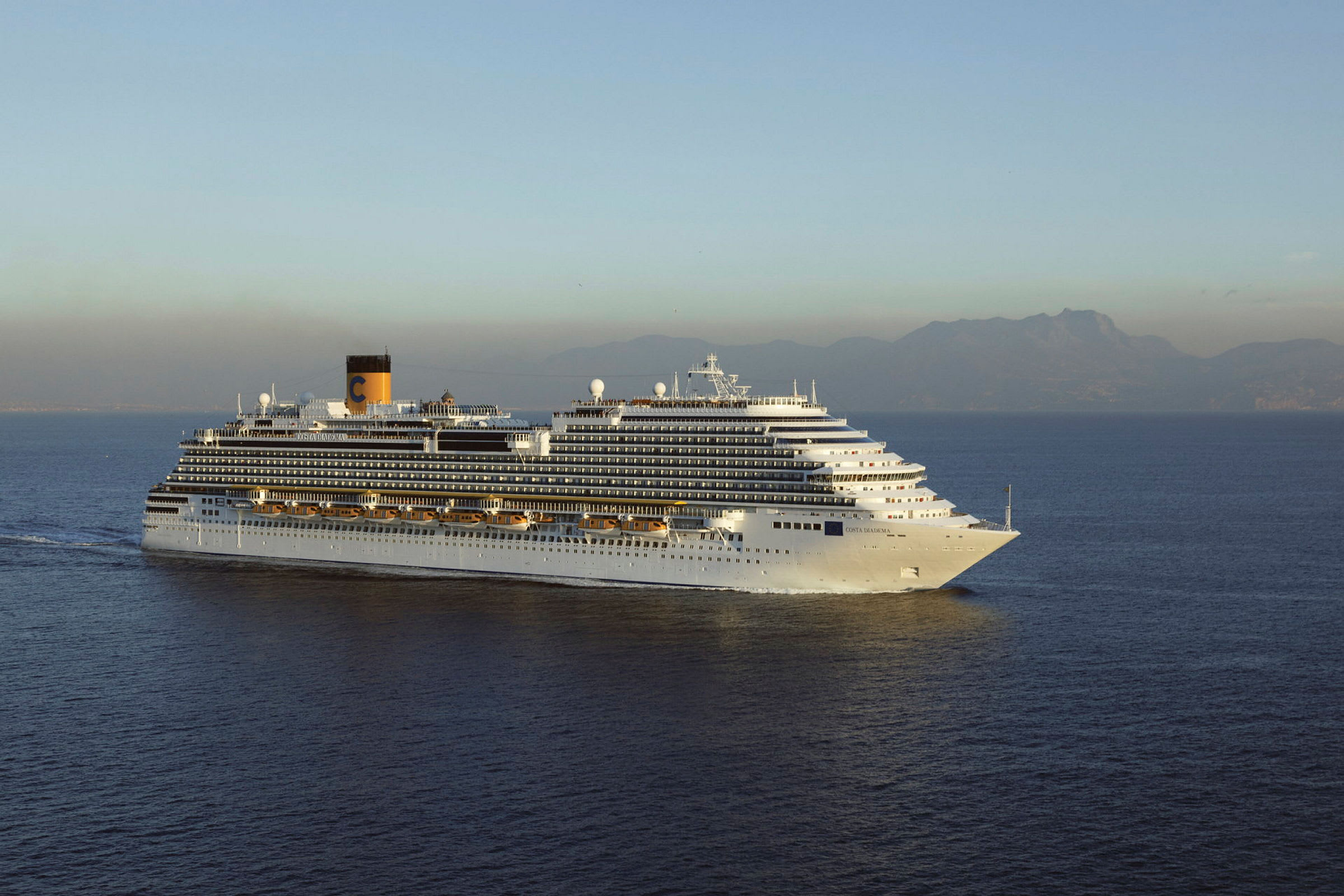 Et cruiseskip seiler på havet med fjell i bakgrunnen. (AI-generert tekst)