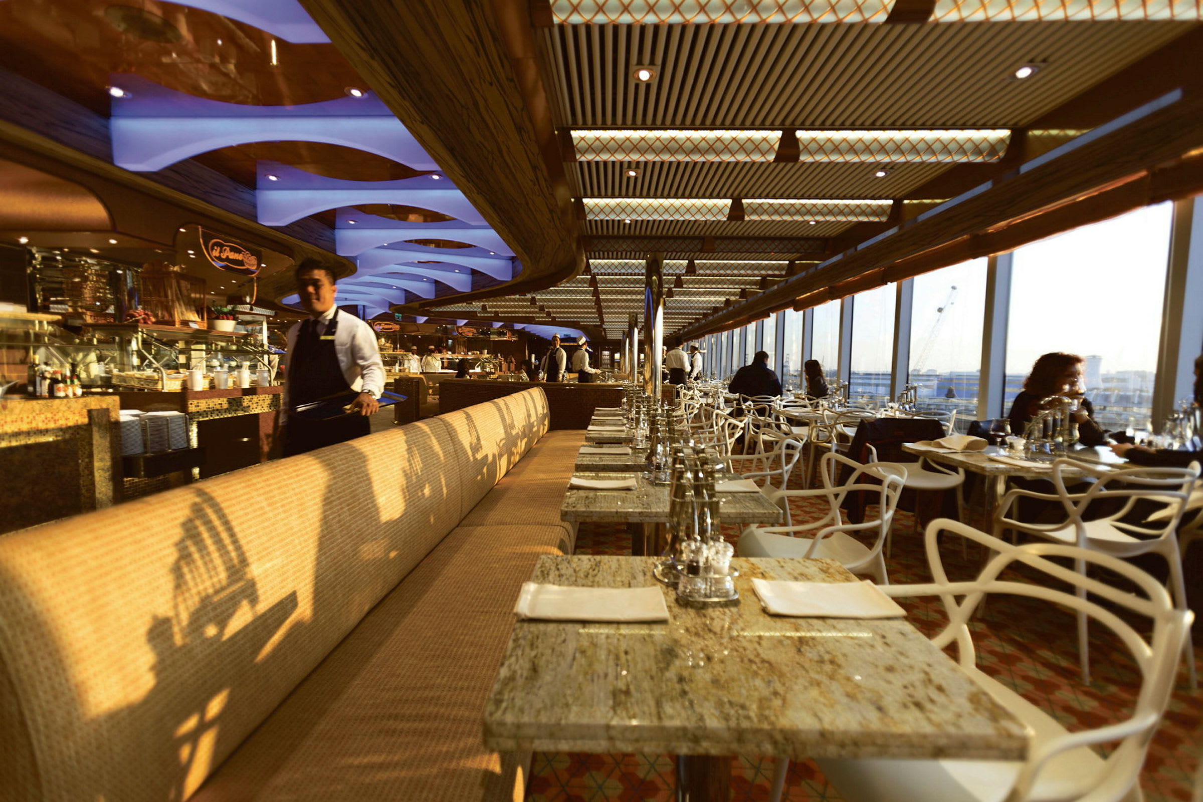 Restaurantmiljø med bord og benker, store vinduer og utsikt over byen. (AI-generert tekst)