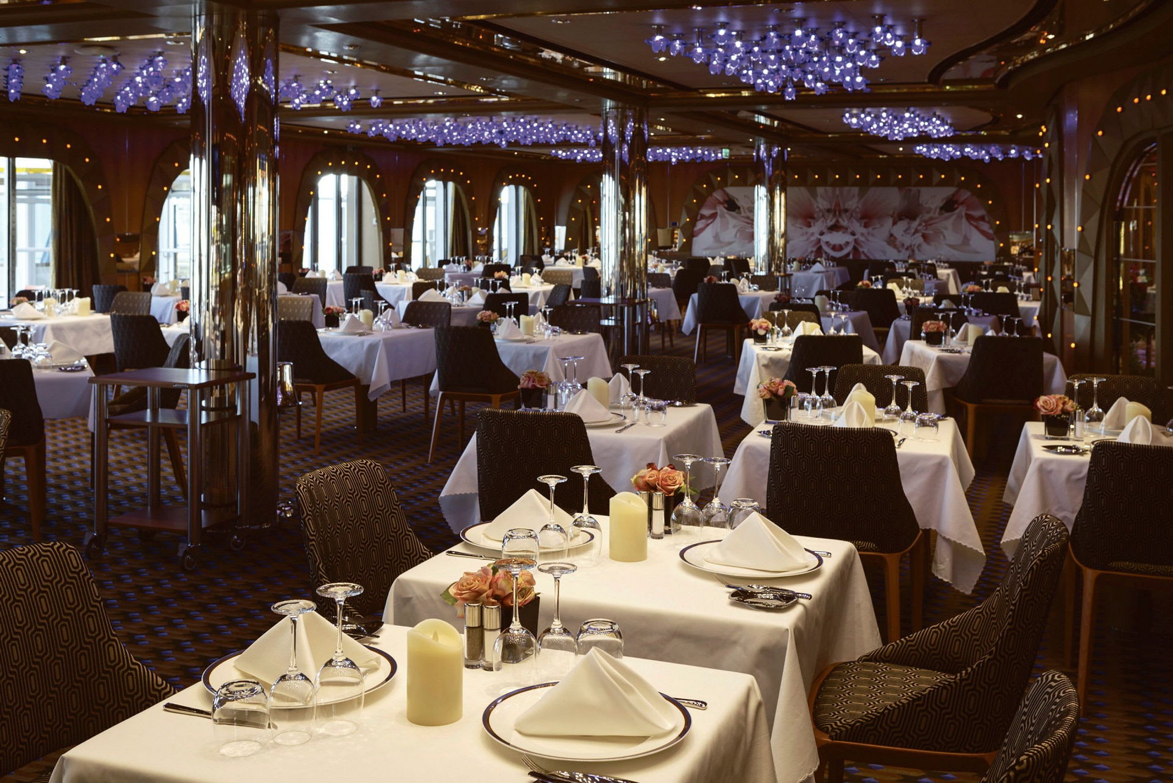 En restaurant med mange bord som er dekket med hvite duker, glass og servise. (AI-generert tekst)