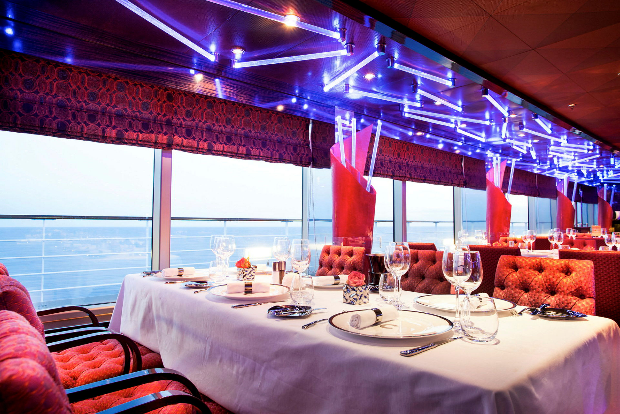 Elegant restaurantinteriør med dekket bord og havutsikt gjennom panoramavinduer. (AI-generert tekst)