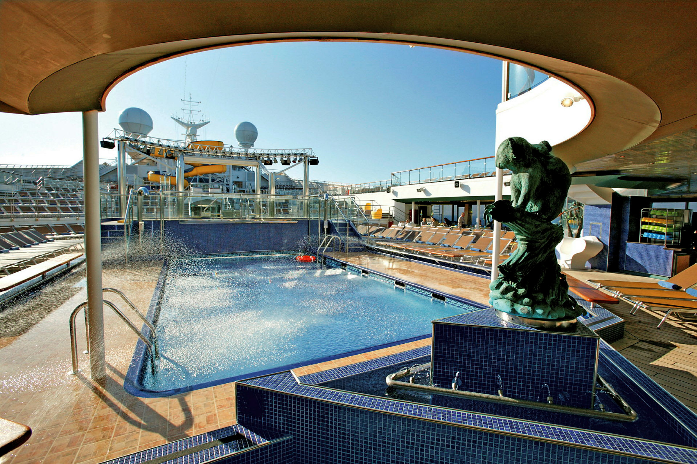 Et blått basseng omgitt av solsenger på dekket av et cruiseskip, med en skulptur i forgrunnen. (AI-generert tekst)