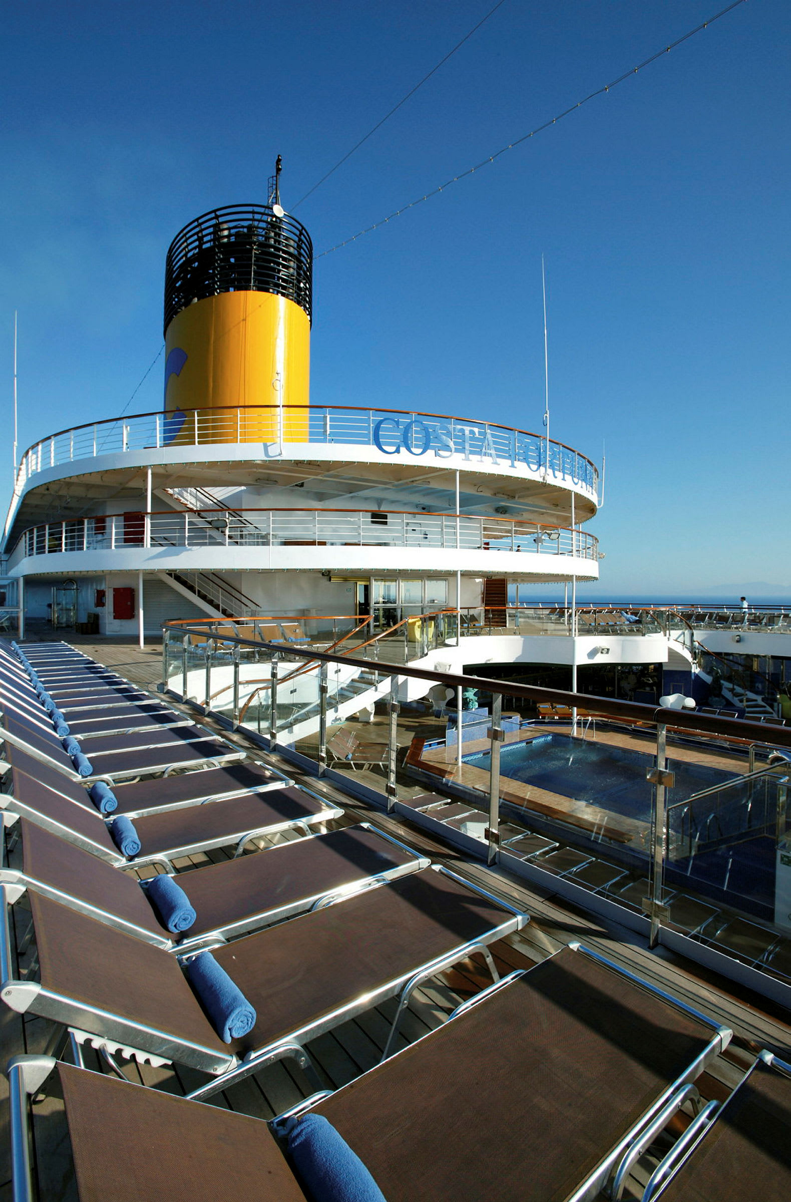 Cruiseskipets soldekk med solsenger og basseng samt skorstein i bakgrunnen. (AI-generert tekst)