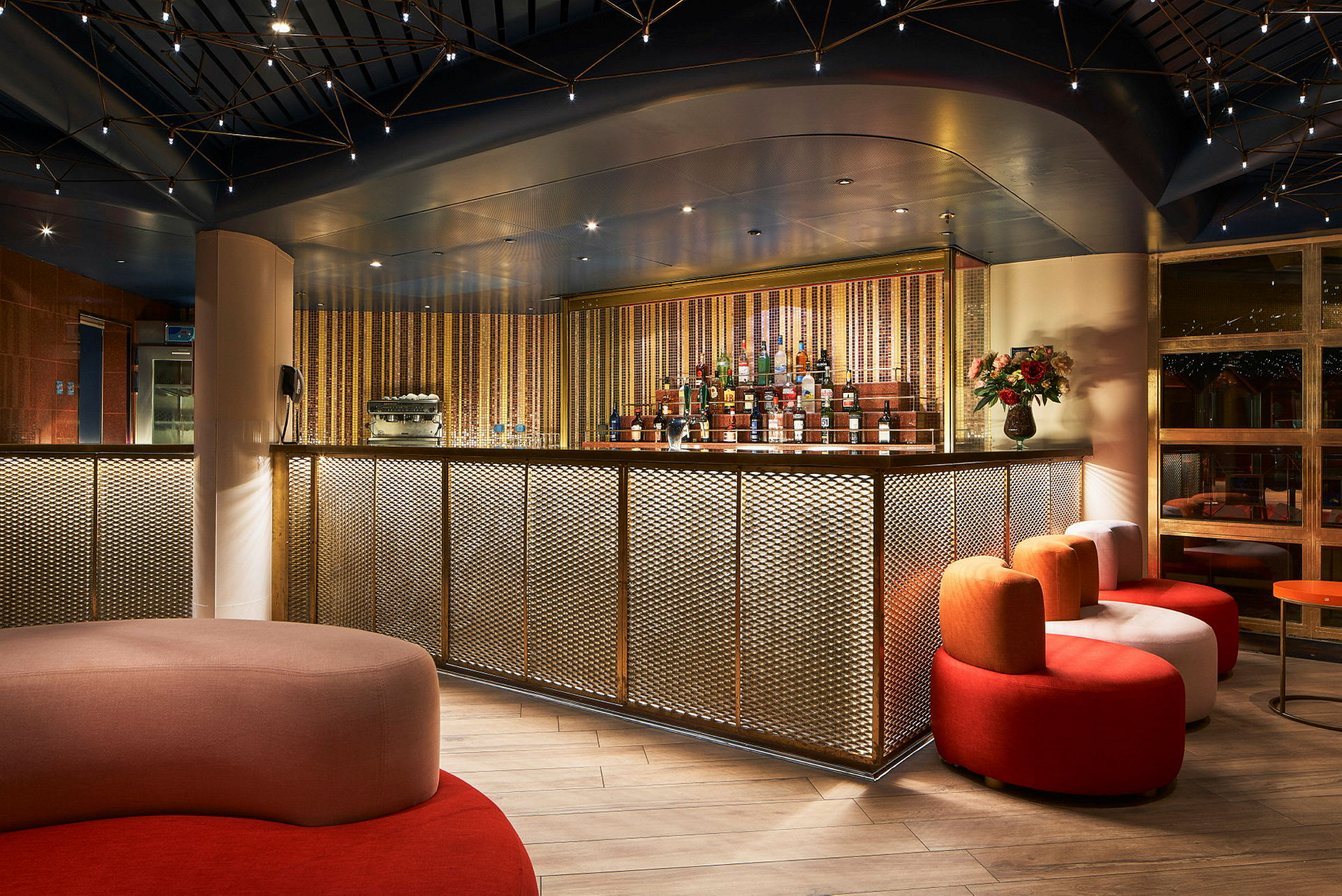 En elegant bar med gulldekorert front, sittemøbler i forskjellige farger og varm belysning. (AI-generert tekst)