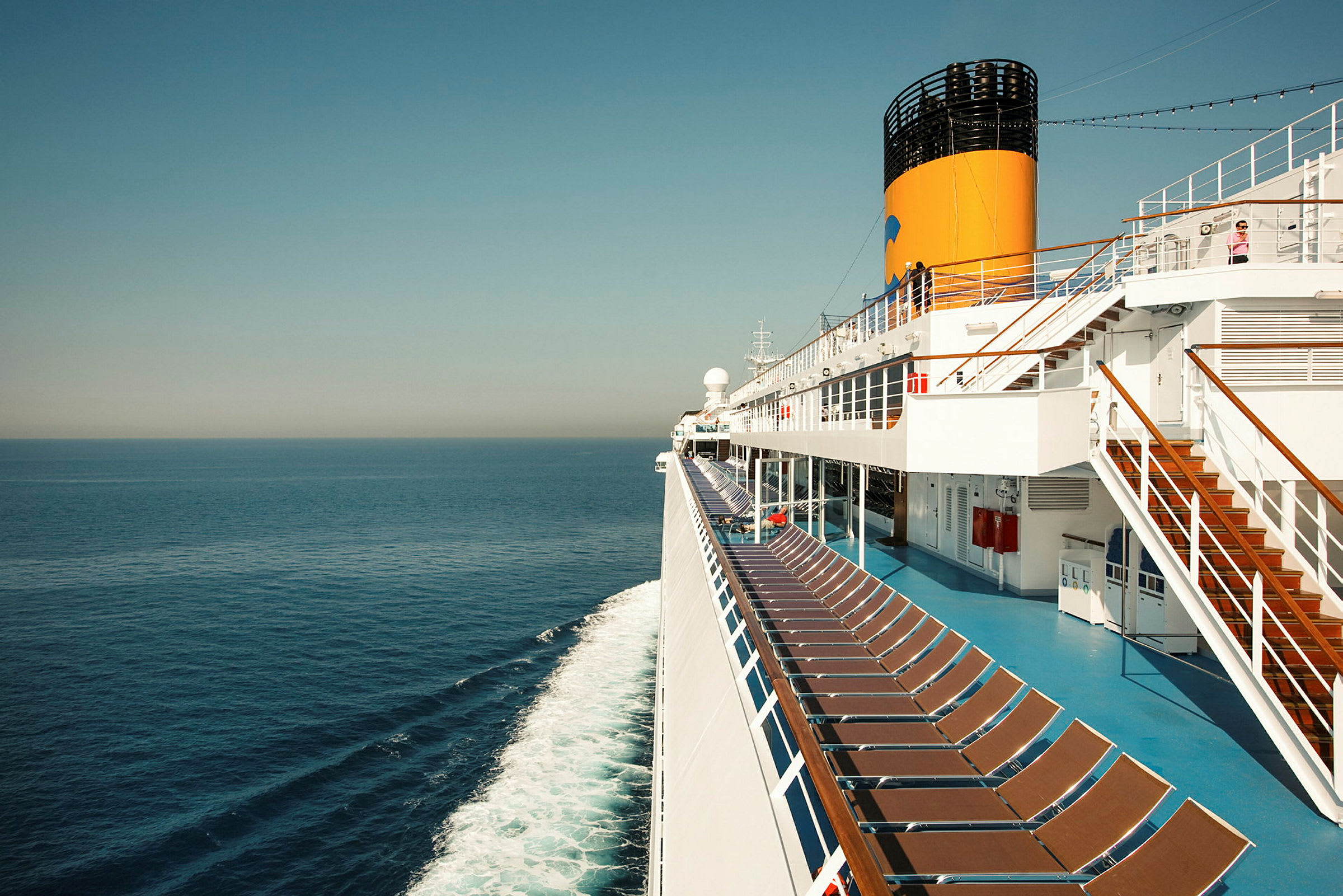 Bilde av dekket på et cruiseskip med solstoler og havet i bakgrunnen. (AI-generert tekst)