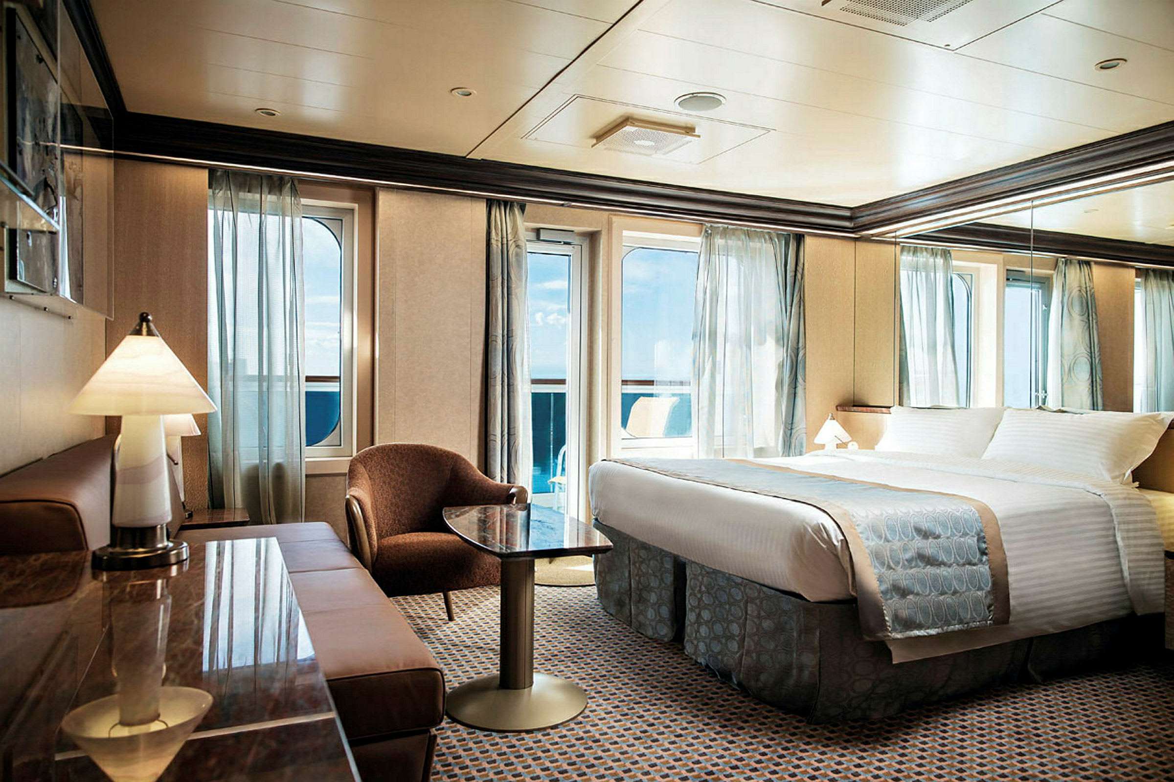 Et hotellrom med en dobbeltseng, sittegruppe og vinduer med utsikt mot havet. (AI-generert tekst)