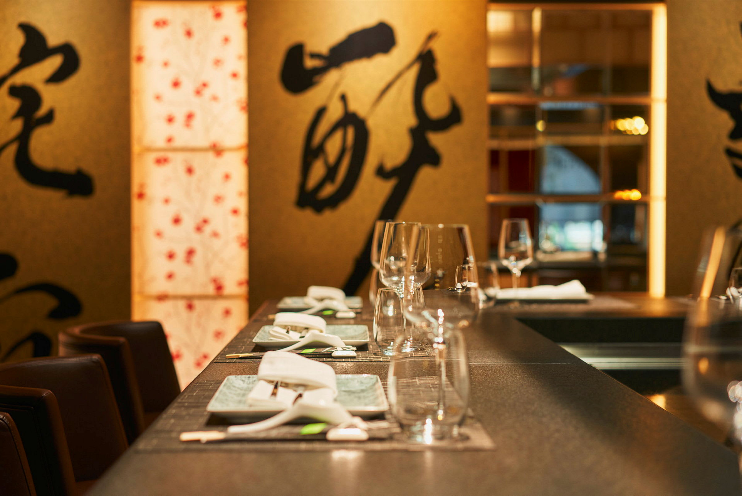 Et dekket bord på en restaurant, dekorert med glass, porselen og bestikk. I bakgrunnen vises dekorasjoner med asiatiske motiv. (AI-generert tekst)