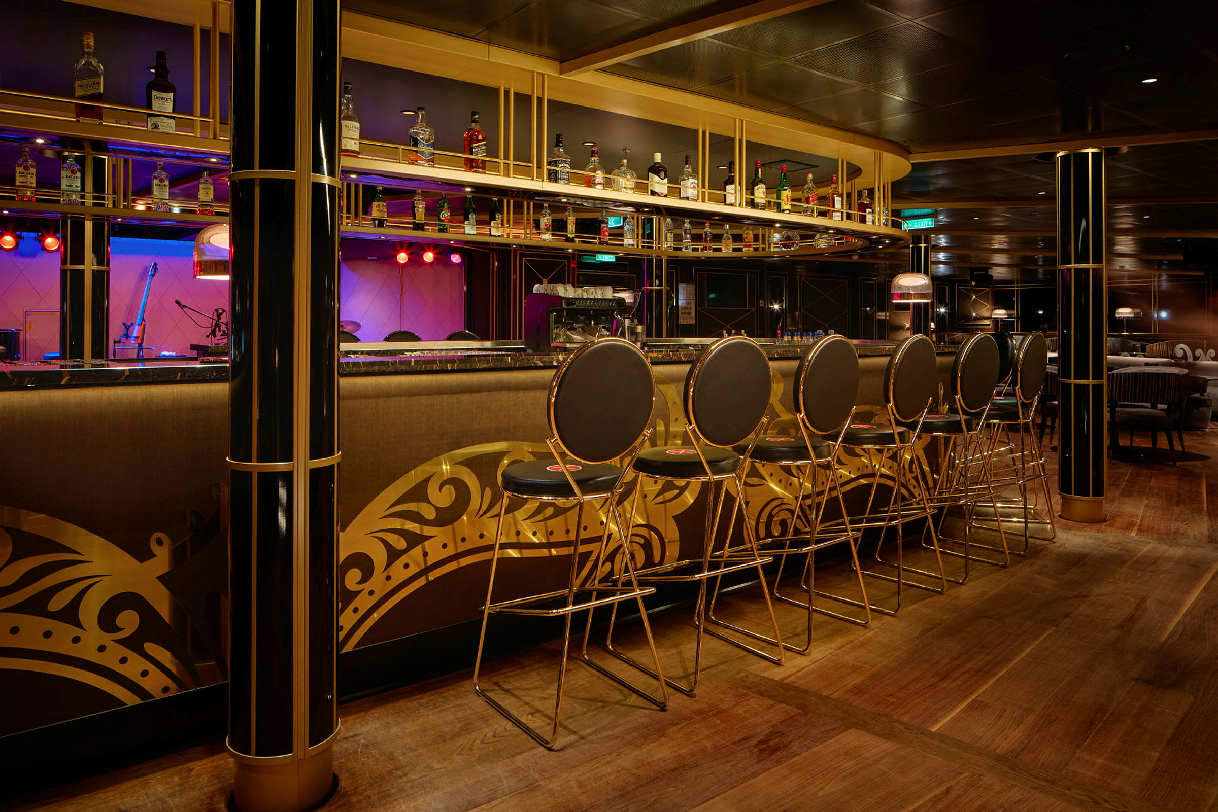 En elegant bar med høye stoler og ei hylle med flasker over bardisken. Interiøret har gyldne dekorasjoner. (AI-generert tekst)