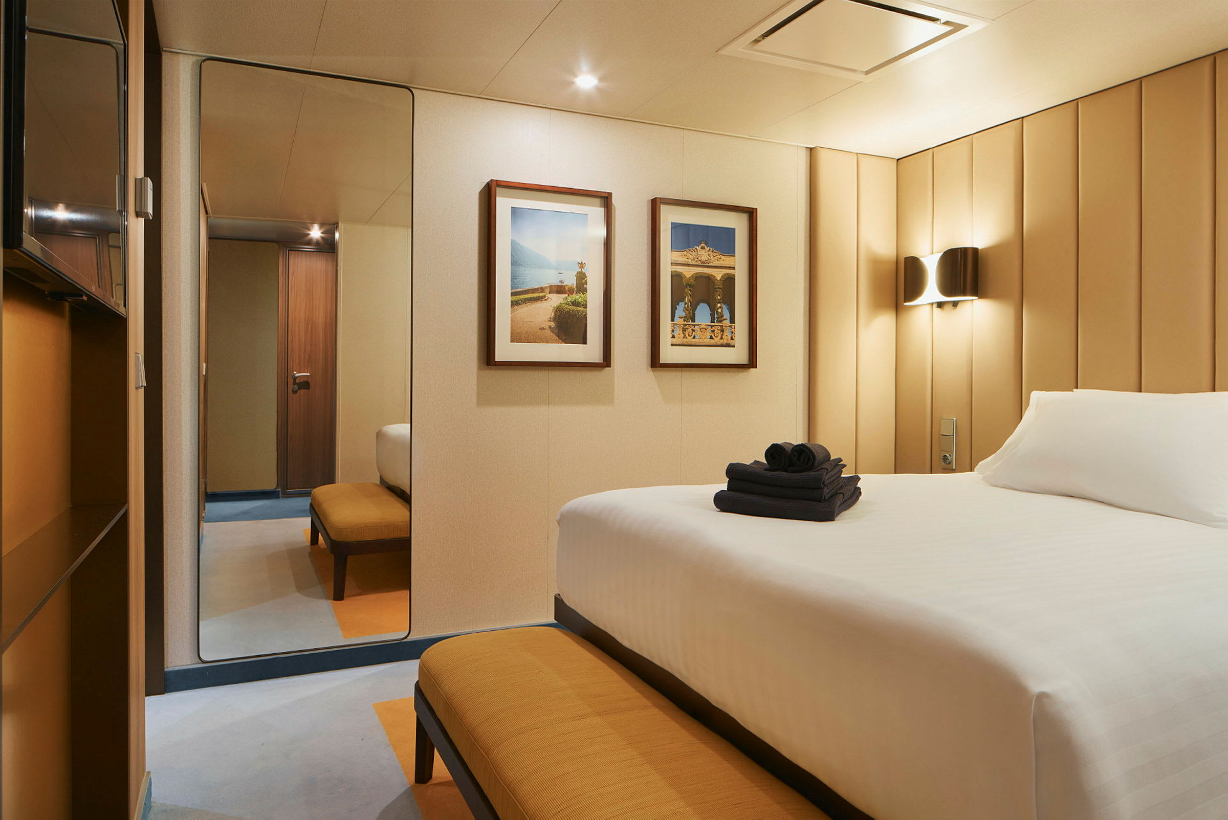 Et hotellrom med en seng, en benk og to bilder på veggen. (AI-generert tekst)