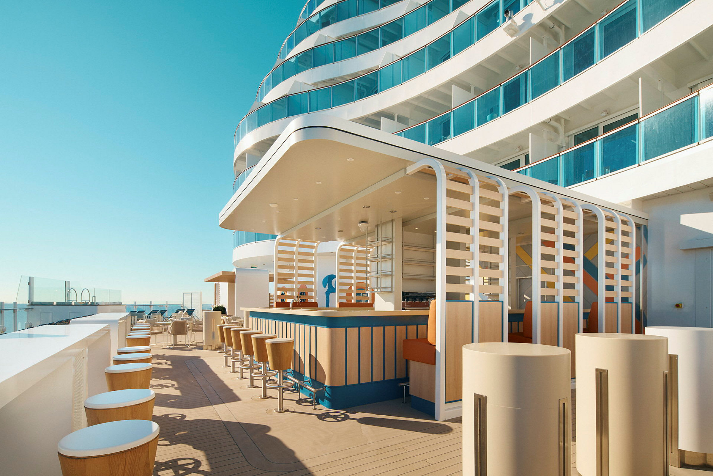 En moderne utendørsbar på et skip med stilige trestoler og en terrasse som vender ut mot en klar himmel. (AI-generert tekst)