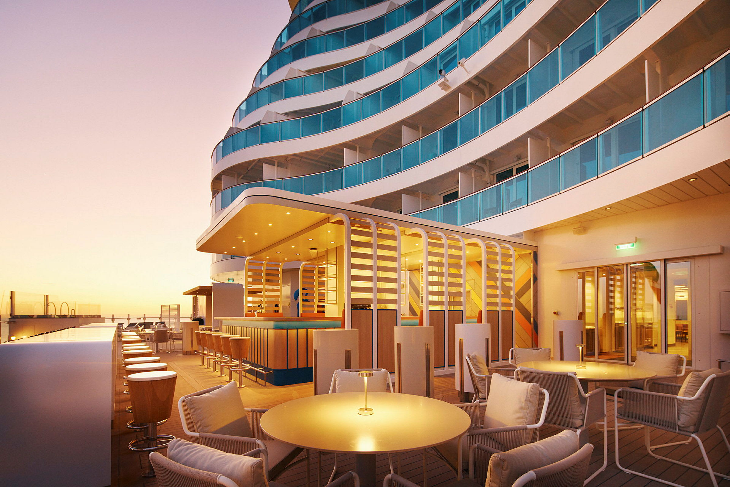 Utendørsområde med sittegrupper, bar og balkonger i solnedgangens lys. (AI-generert tekst)