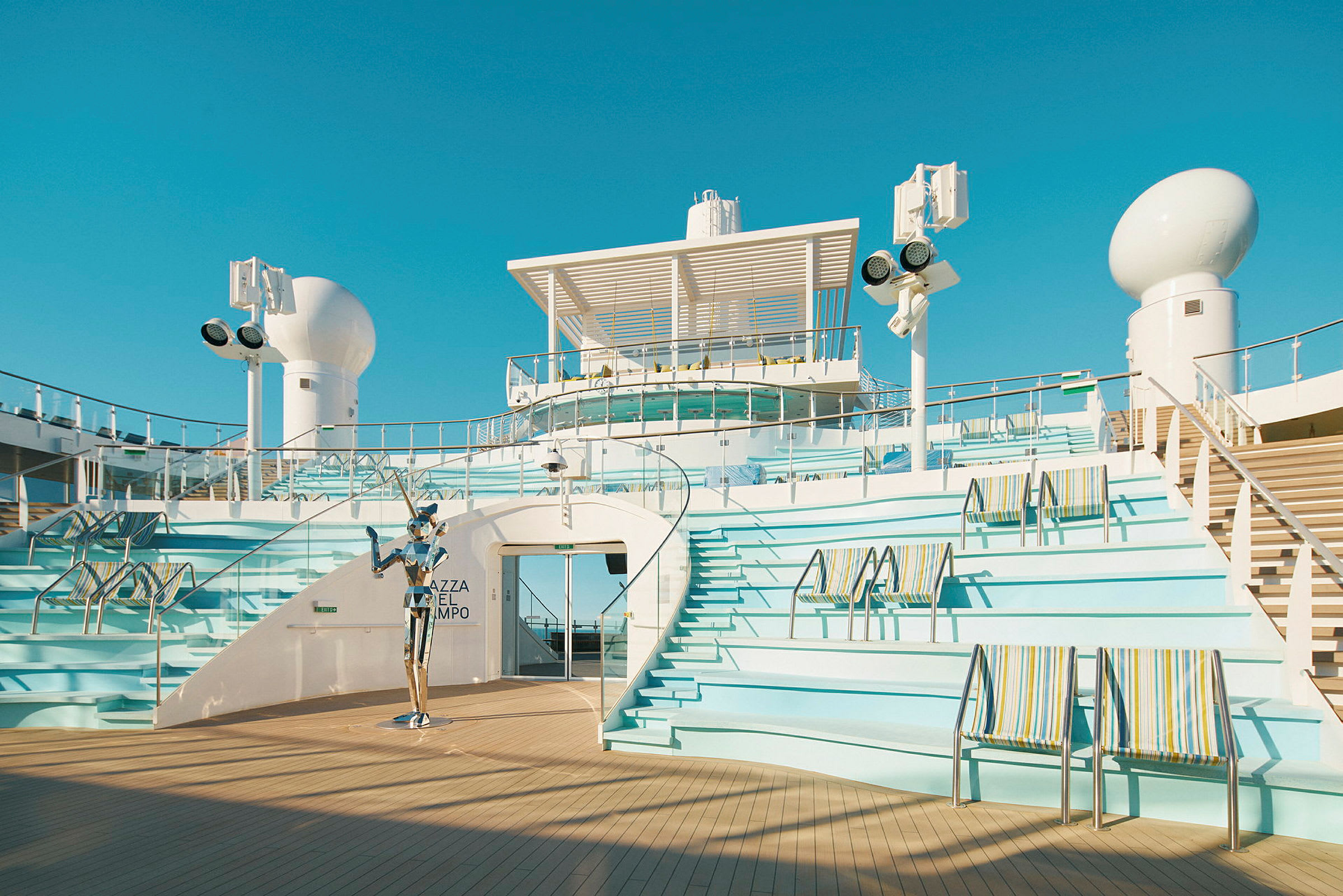 Åpent soldekkmiljø på cruiseskip, med sitteplasser, trapper og kunstinstallasjon. (AI-generert tekst)