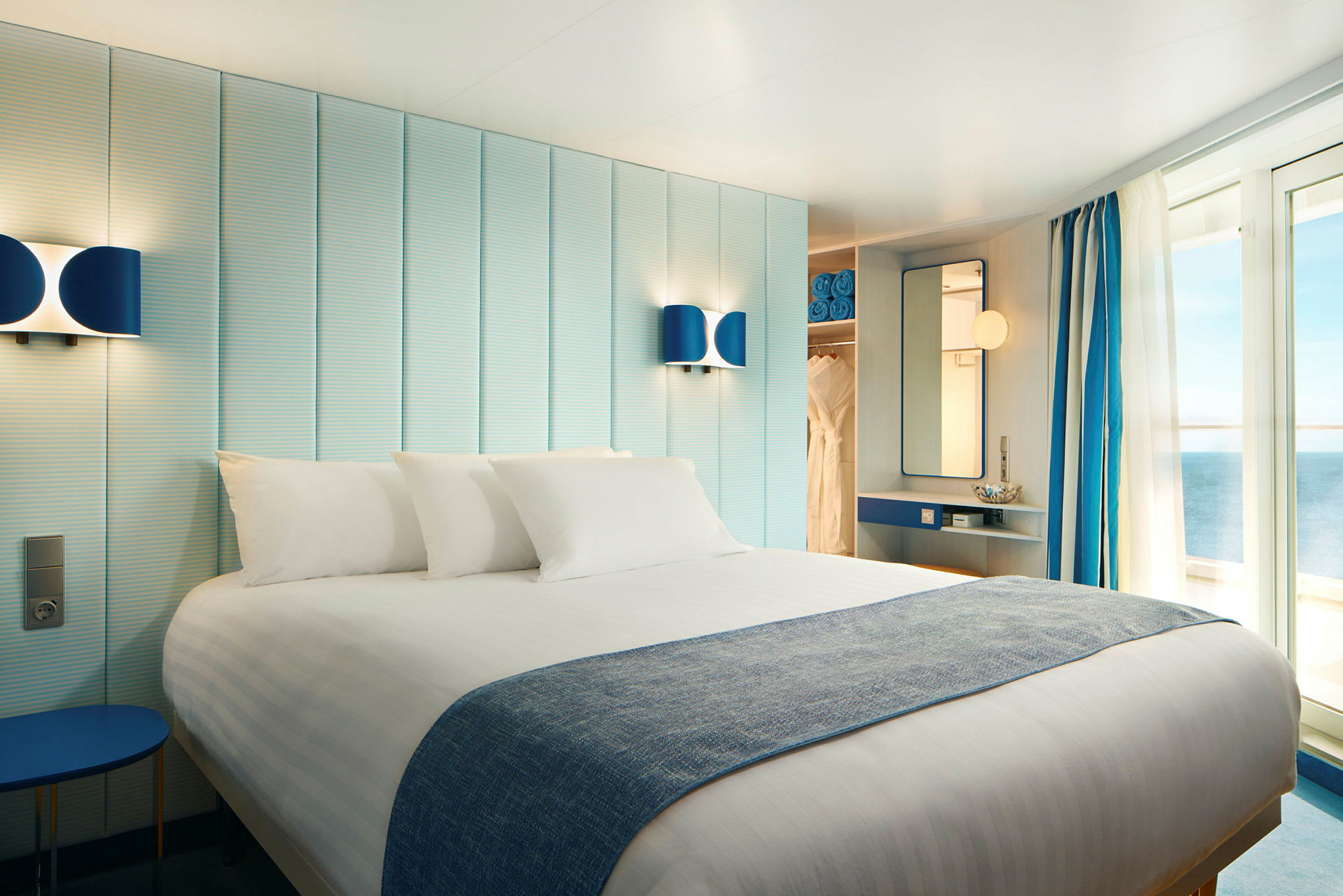 Et hotellrom med en dobbeltseng, lys innredning og balkongdører som vender mot havet. (AI-generert tekst)