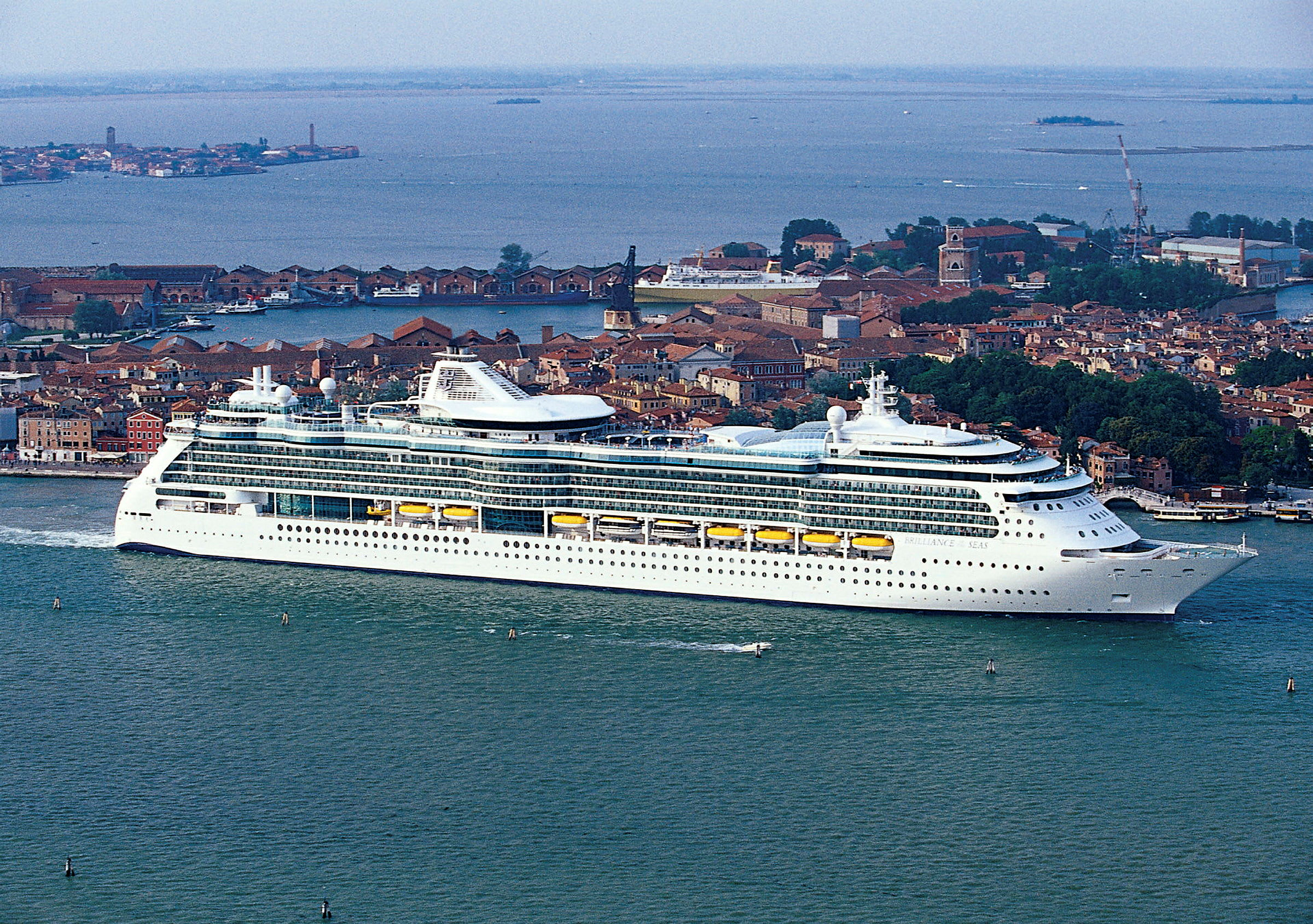Et cruiseskip foran en by ved sjøen. (AI-generert tekst)