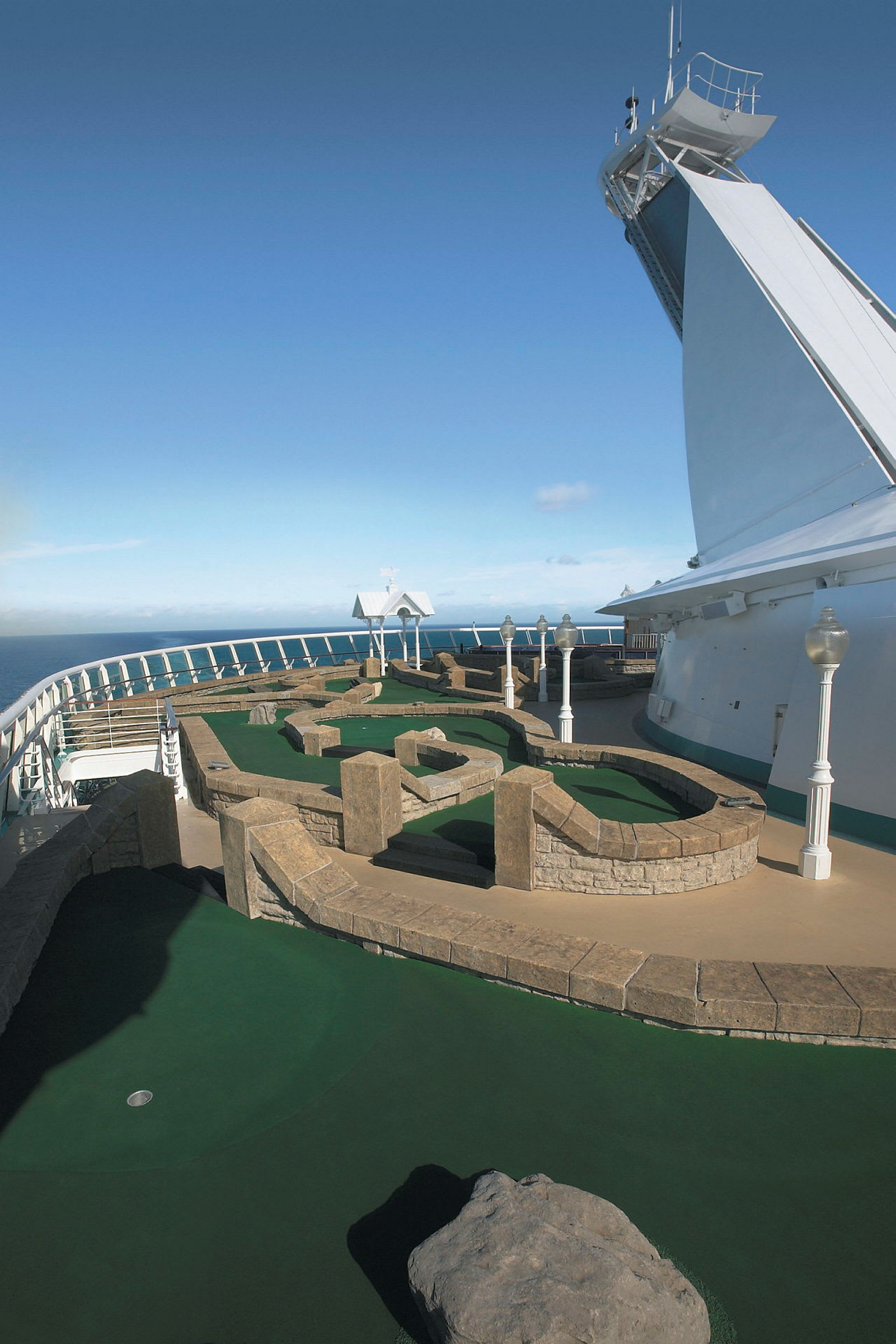 Minigolfbane med kunstgress og steinbarrierer på et skip med havet i bakgrunnen. (AI-generert tekst)