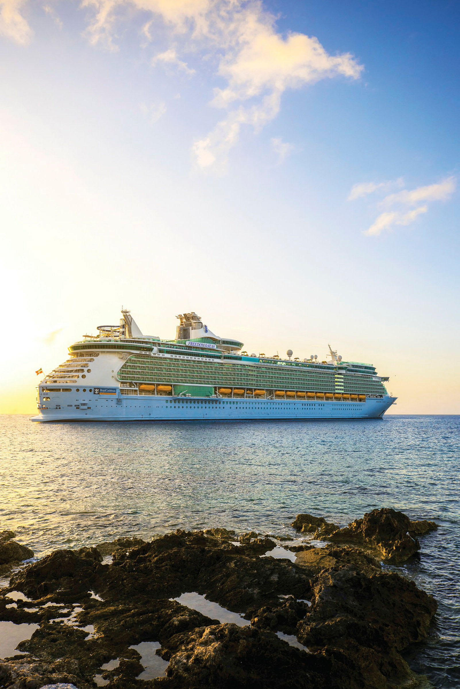 Bilde av et stort cruiseskip på havet med steiner i forgrunnen og himmelen i kveldslys. (AI-generert tekst)
