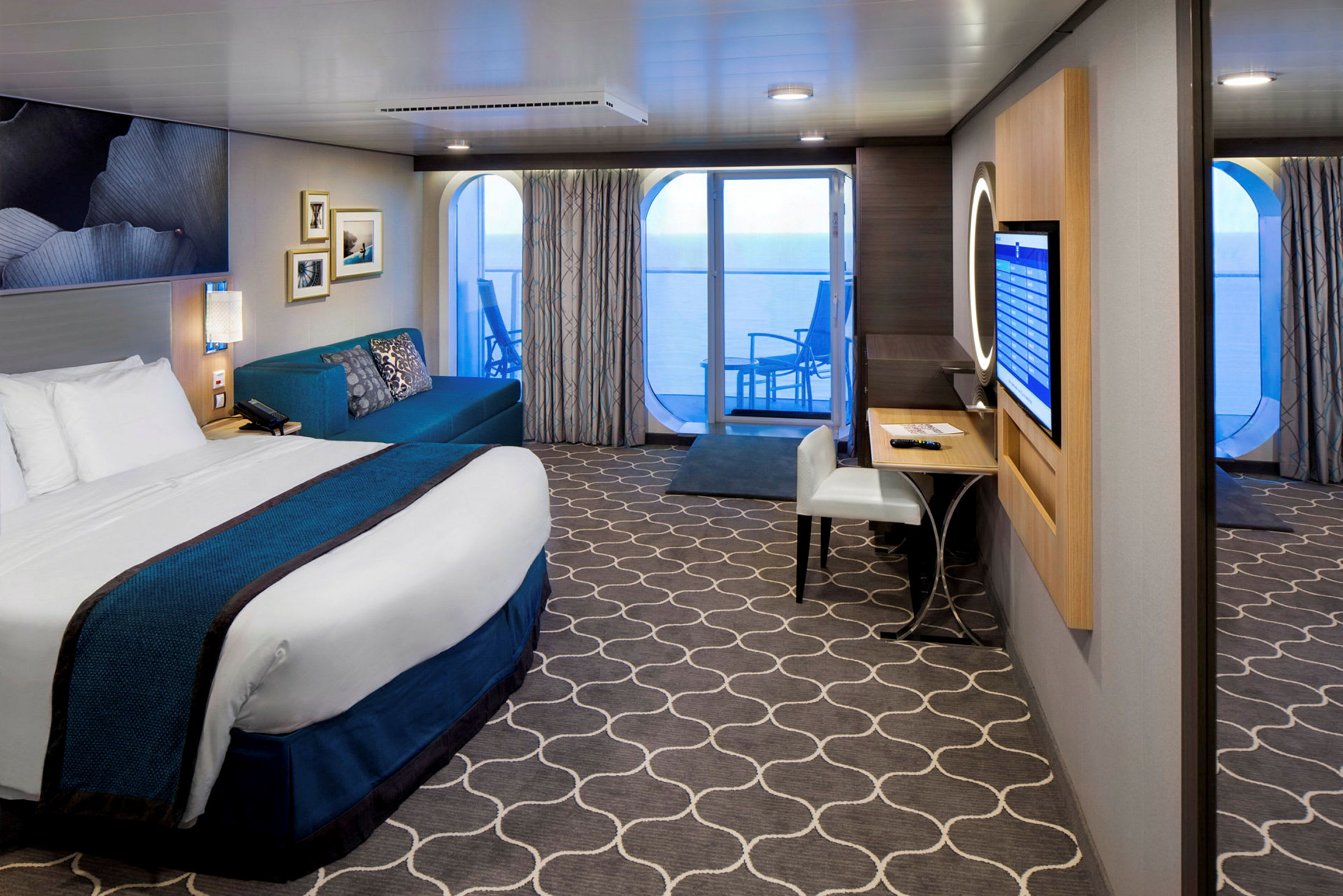 Et hotellrom med seng, sofa, skrivebord og balkong med utsikt over havet. (AI-generert tekst)