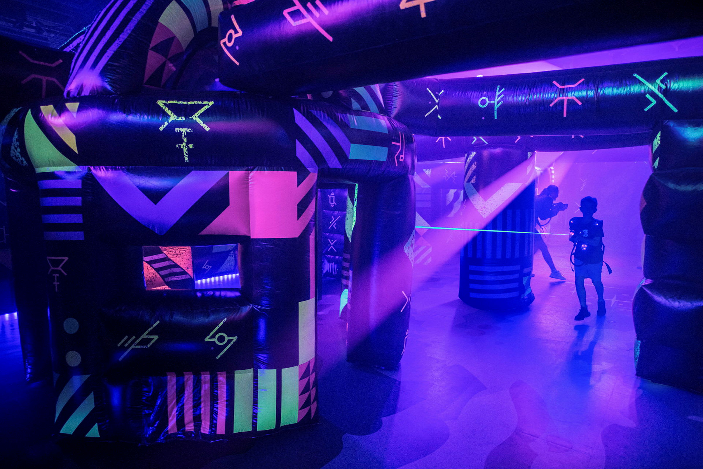 Et neonopplyst innemiljø med oppblåste konstruksjoner og personer som spiller laser tag. (AI-generert tekst)