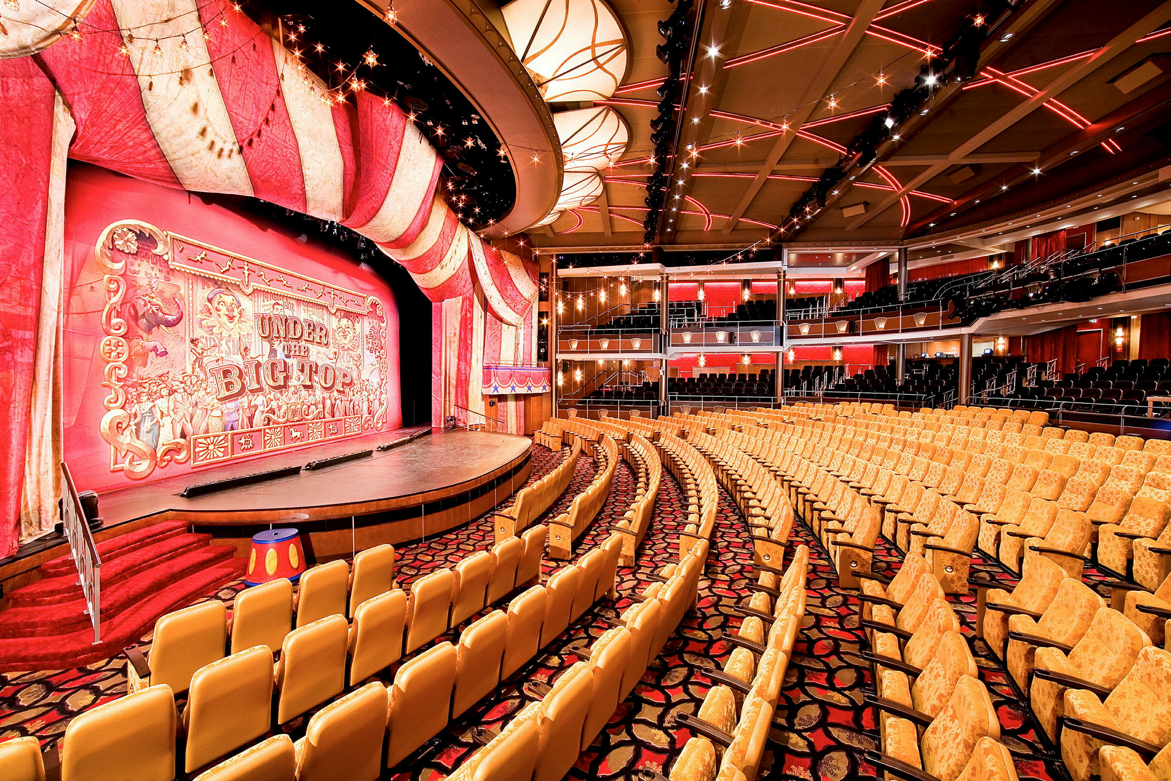 En teatersal med røde og gule dekorasjoner rundt scenen og seter for publikum. (AI-generert tekst)