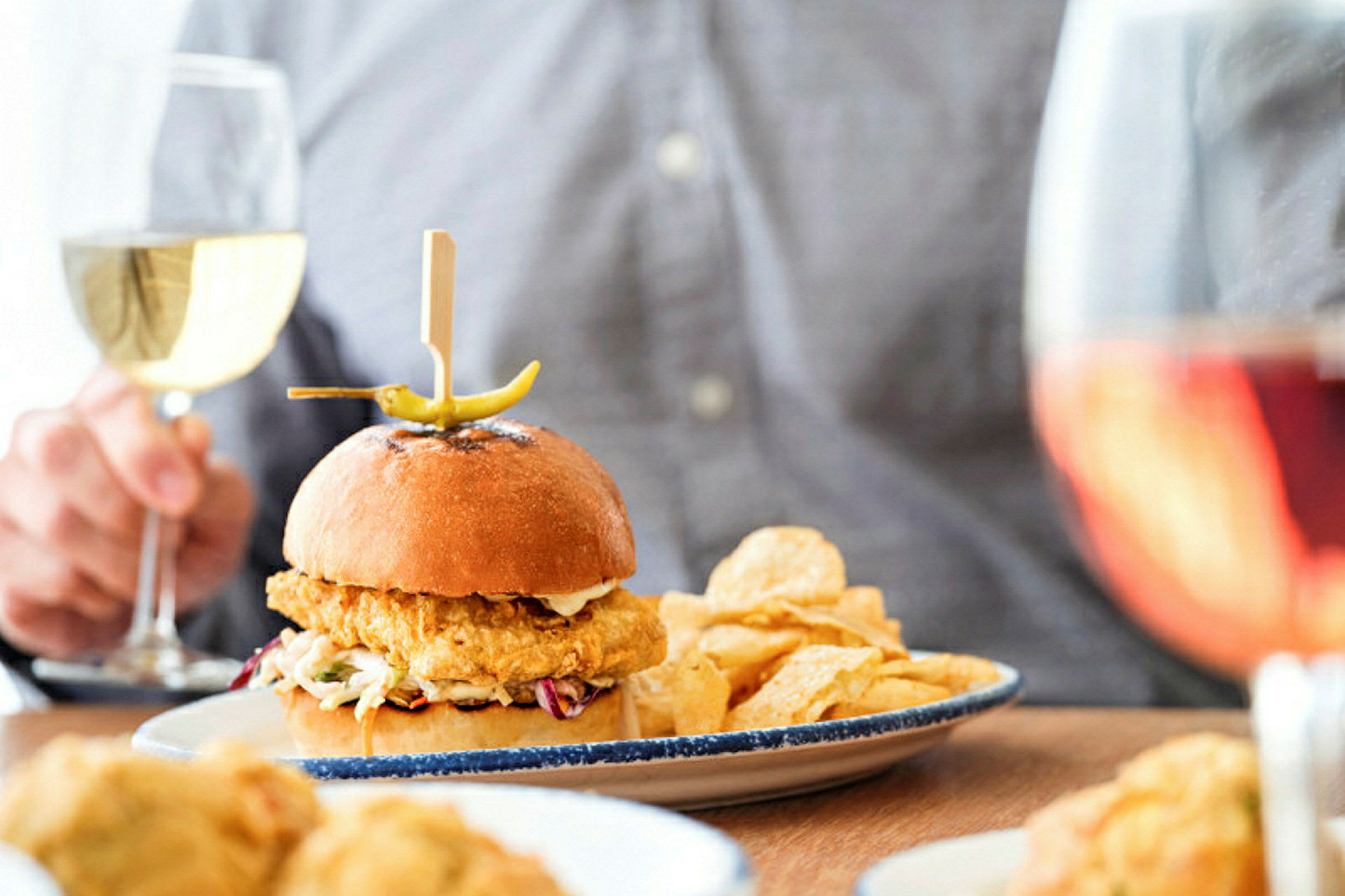 En tallerken med en hamburger, chips og et glass vin vises på bildet. (AI-generert tekst)
