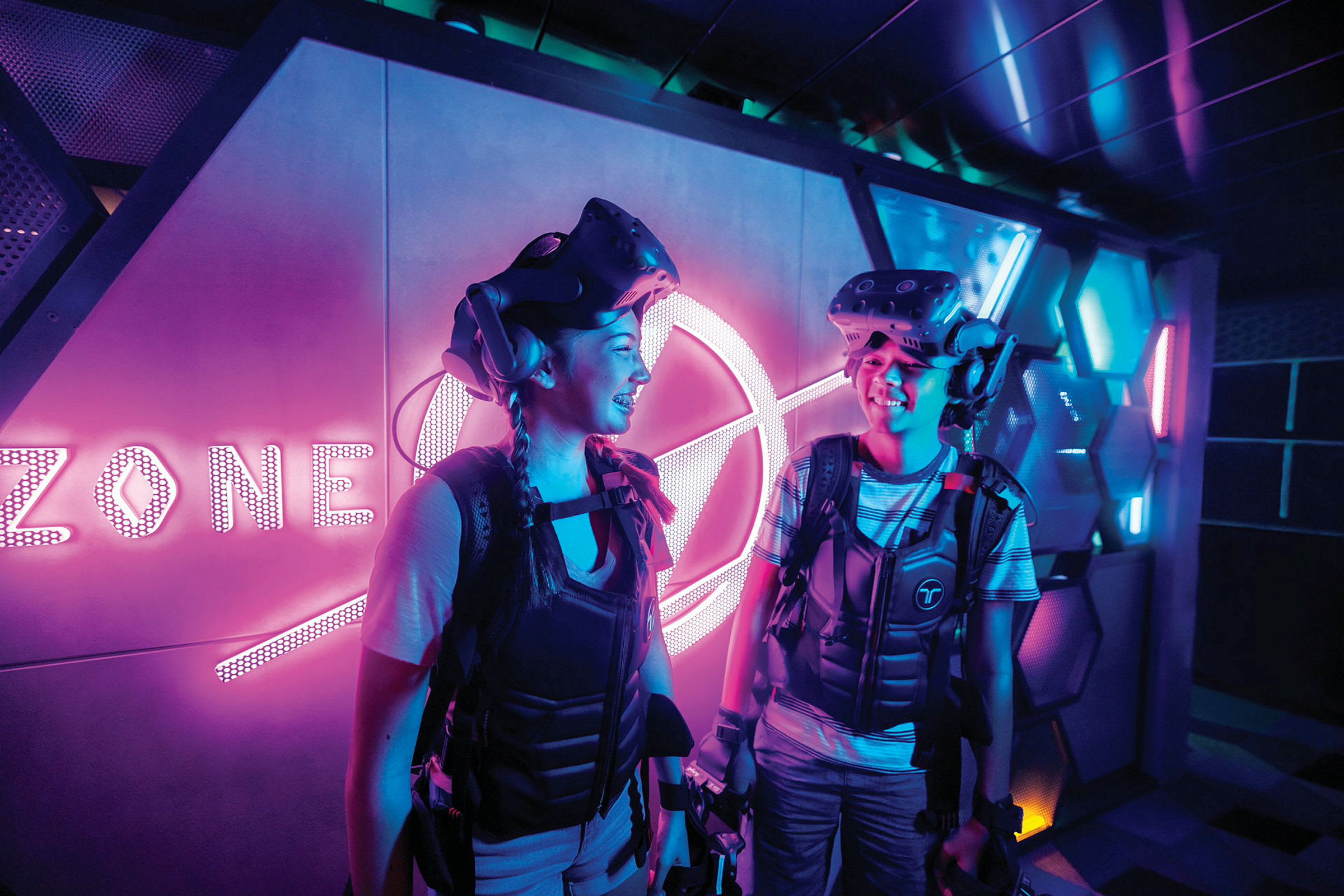 To personer i en futuristisk setting med VR-utstyr og neonbelysning. (AI-generert tekst)