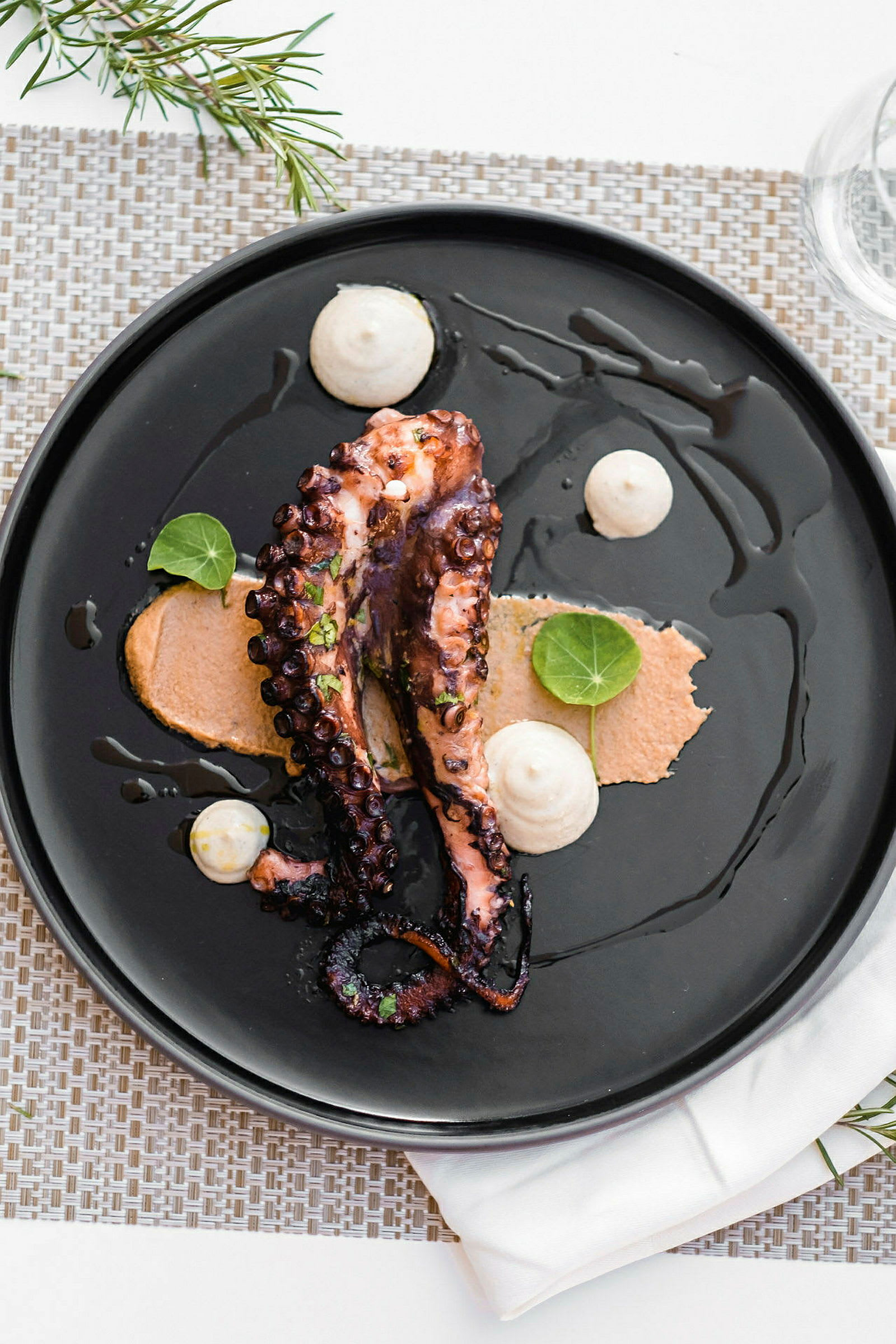 En tallerken med en servering av grillet blekksprut med saus og dekorative blader. (AI-generert tekst)