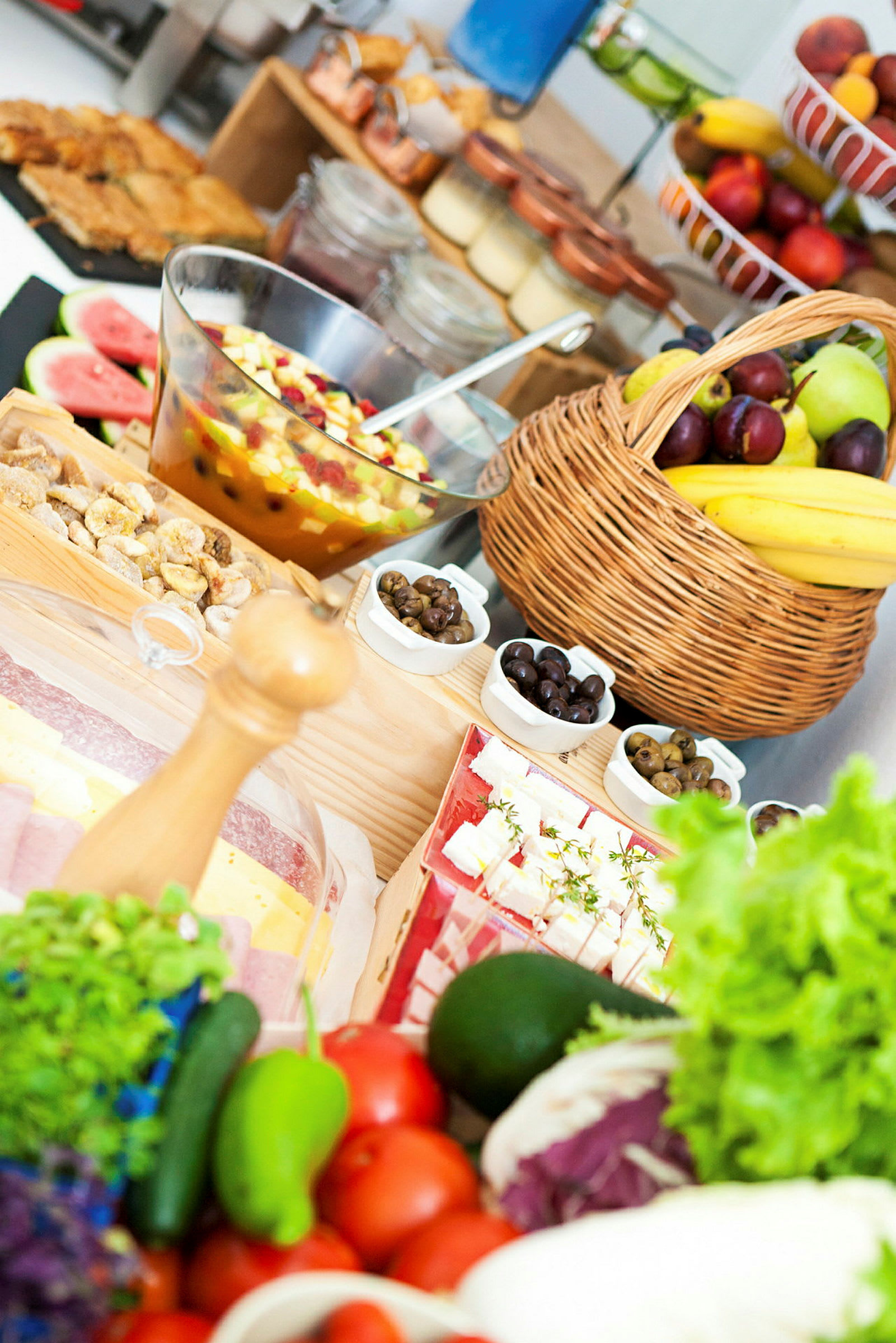 Et bord fylt med ulike ferske frukter, grønnsaker og mat, inkludert en fruktsalat i en glassbolle og en kurv med bananer og plommer. (AI-generert tekst)