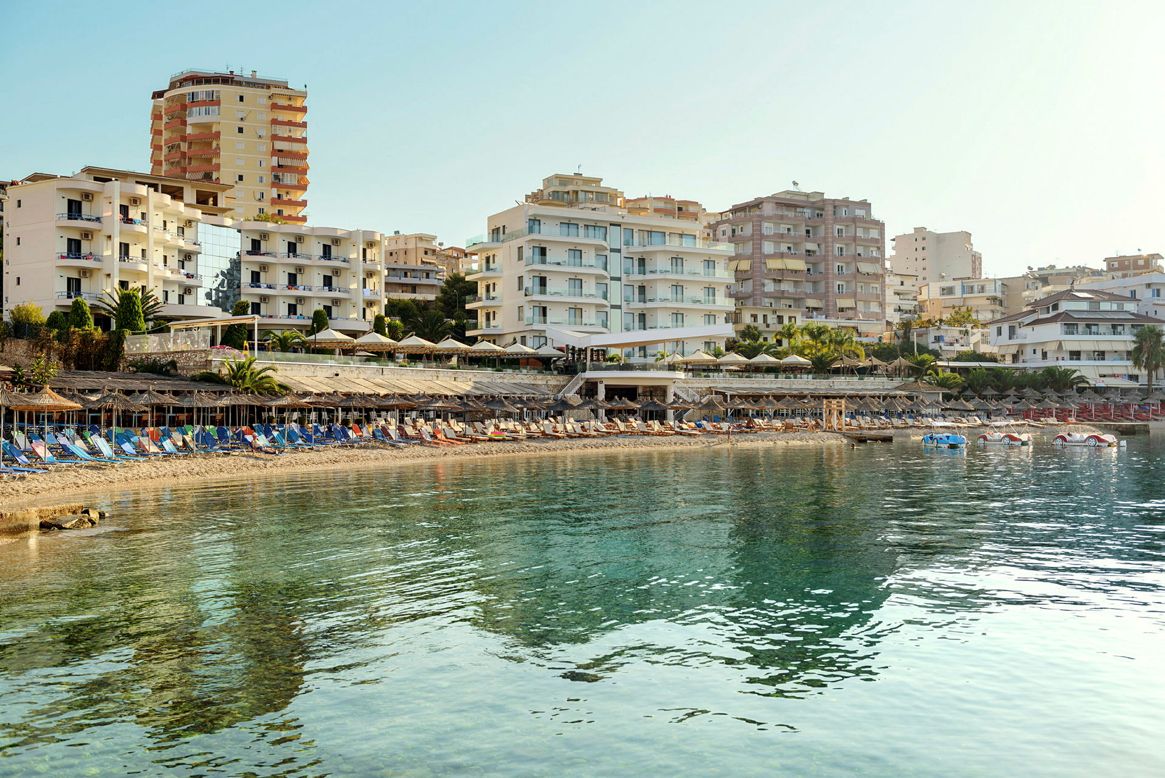 Strand med solsenger og parasoller foran hotellbygninger. (AI-generert tekst)