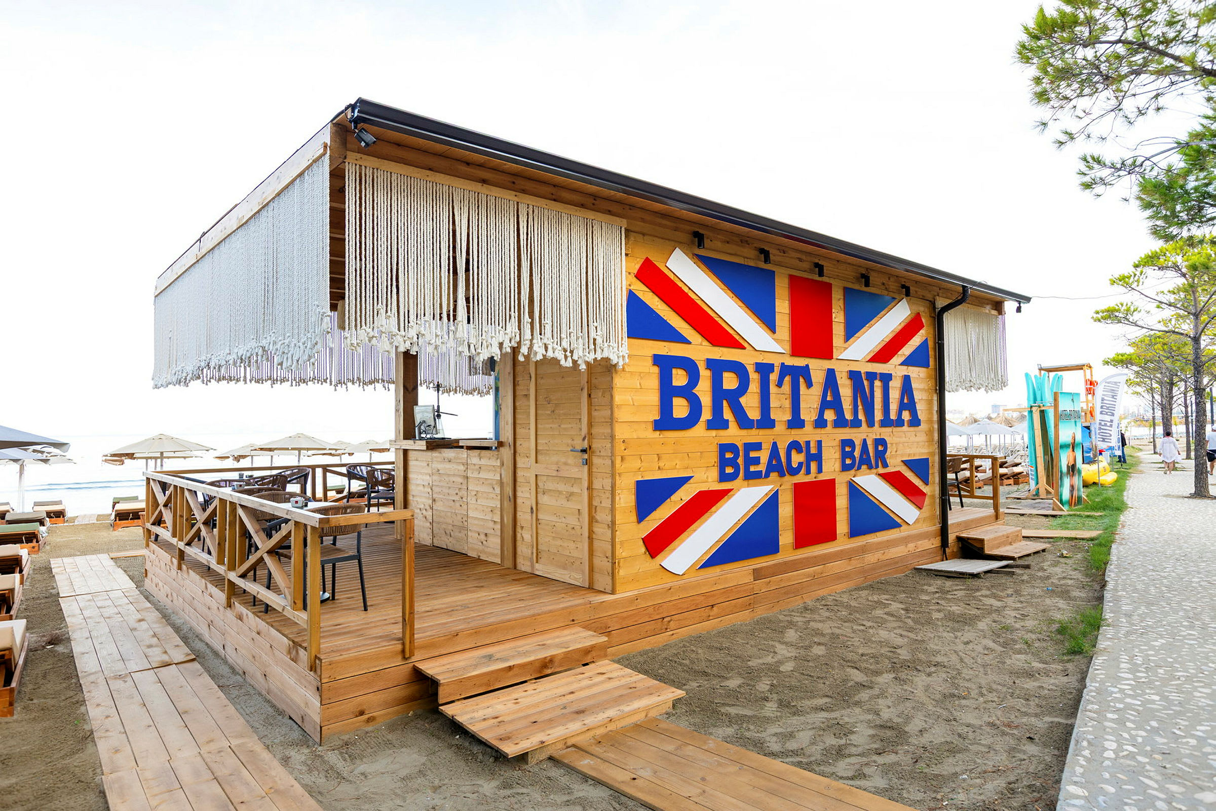 En strandbar med navnet Britania Beach Bar, bygget i tre med dekorasjoner og sitteplasser. (AI-generert tekst)