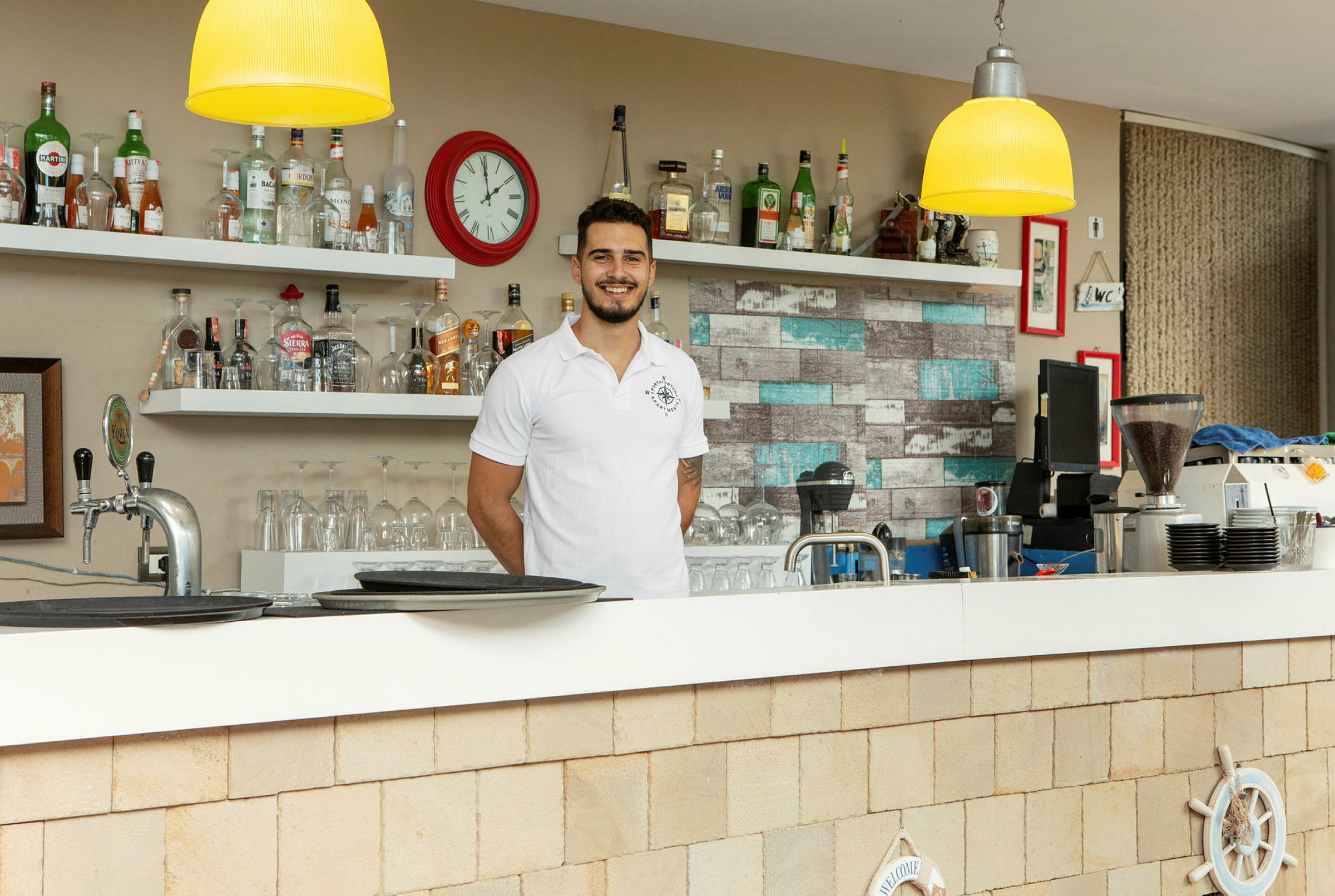 En bar med hyller fulle av flasker og en klokke på veggen. (AI-generert tekst)