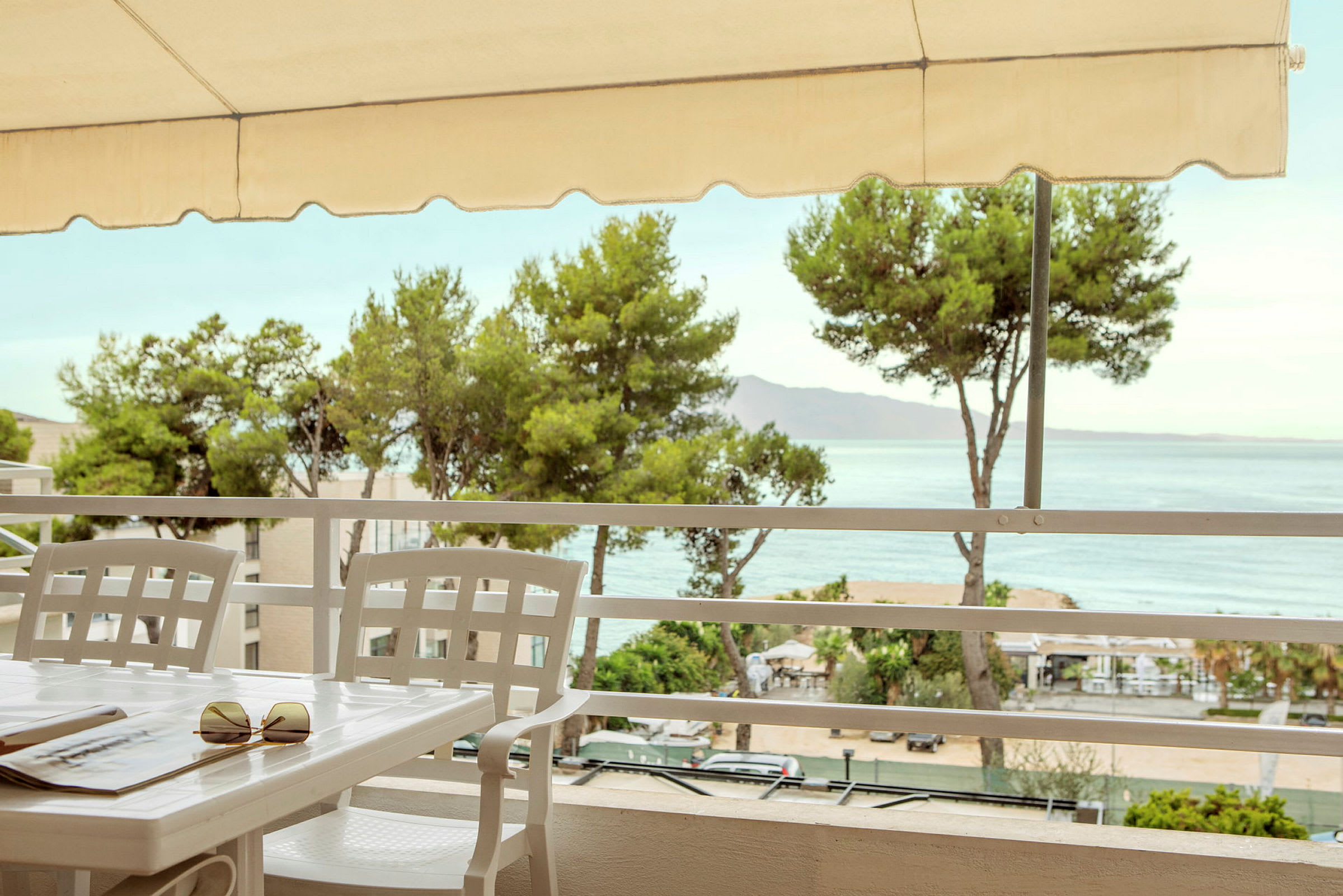 Bord og stoler på en terrasse med utsikt over havet og omkringliggende trær. (AI-generert tekst)