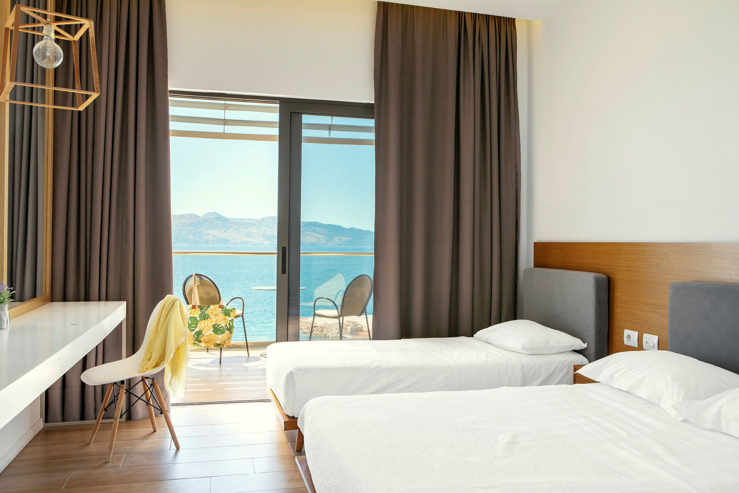 Hotellrom med to enkeltsenger og tilgang til en balkong med utsikt over havet. (AI-generert tekst)