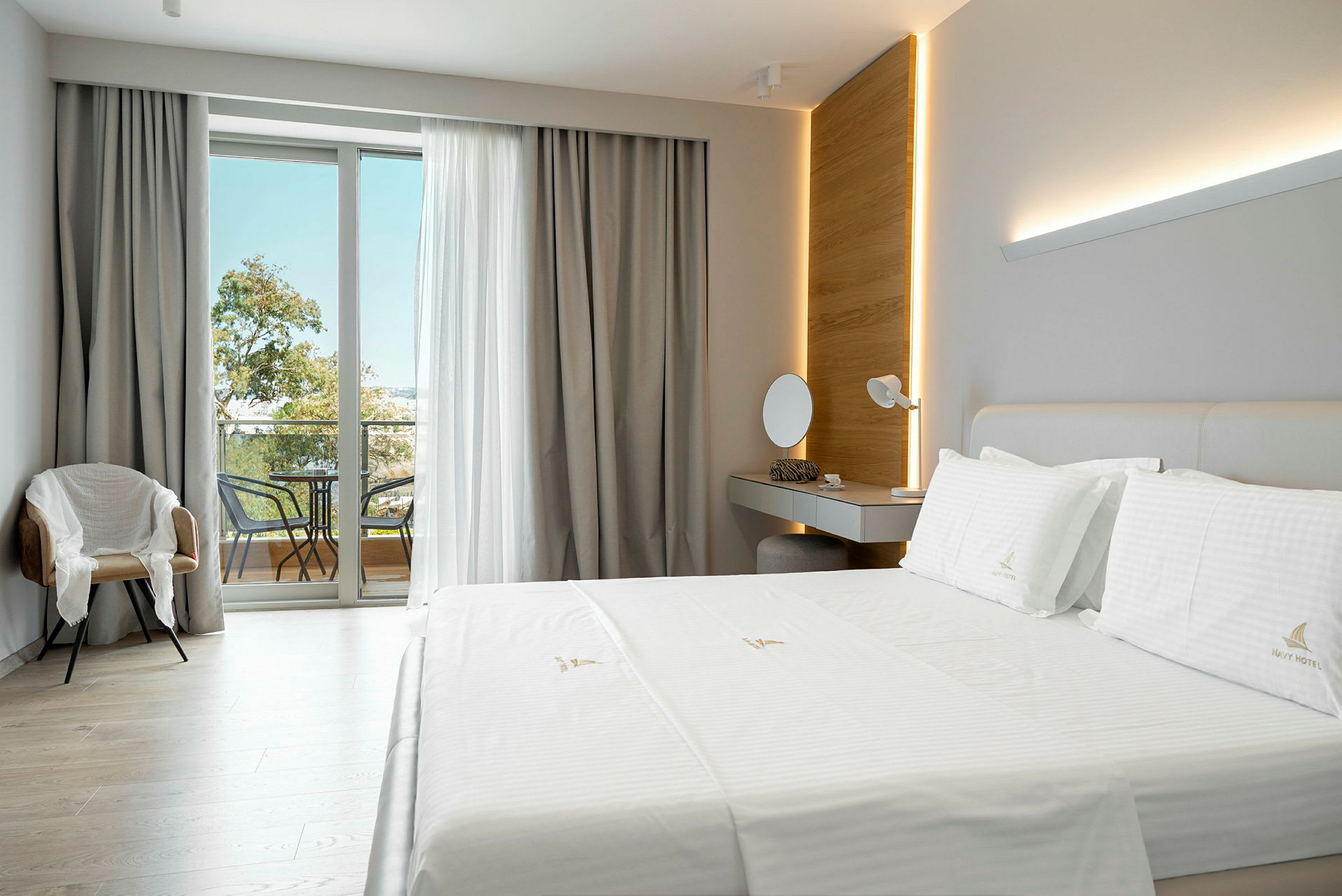 Et moderne hotellrom med en stor seng, et skrivebord, en stol og en balkong med møbler. (AI-generert tekst)