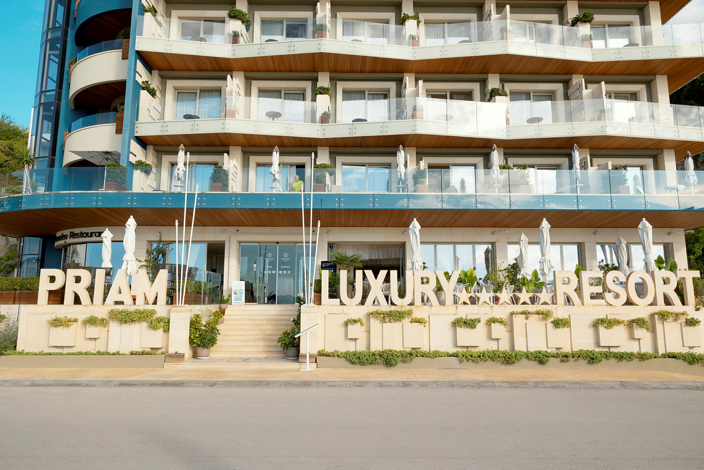 Flere etasjer av et hotell designet i moderne arkitektur med et fremtredende skilt som sier 'Priam Luxury Resort'. (AI-generert tekst)