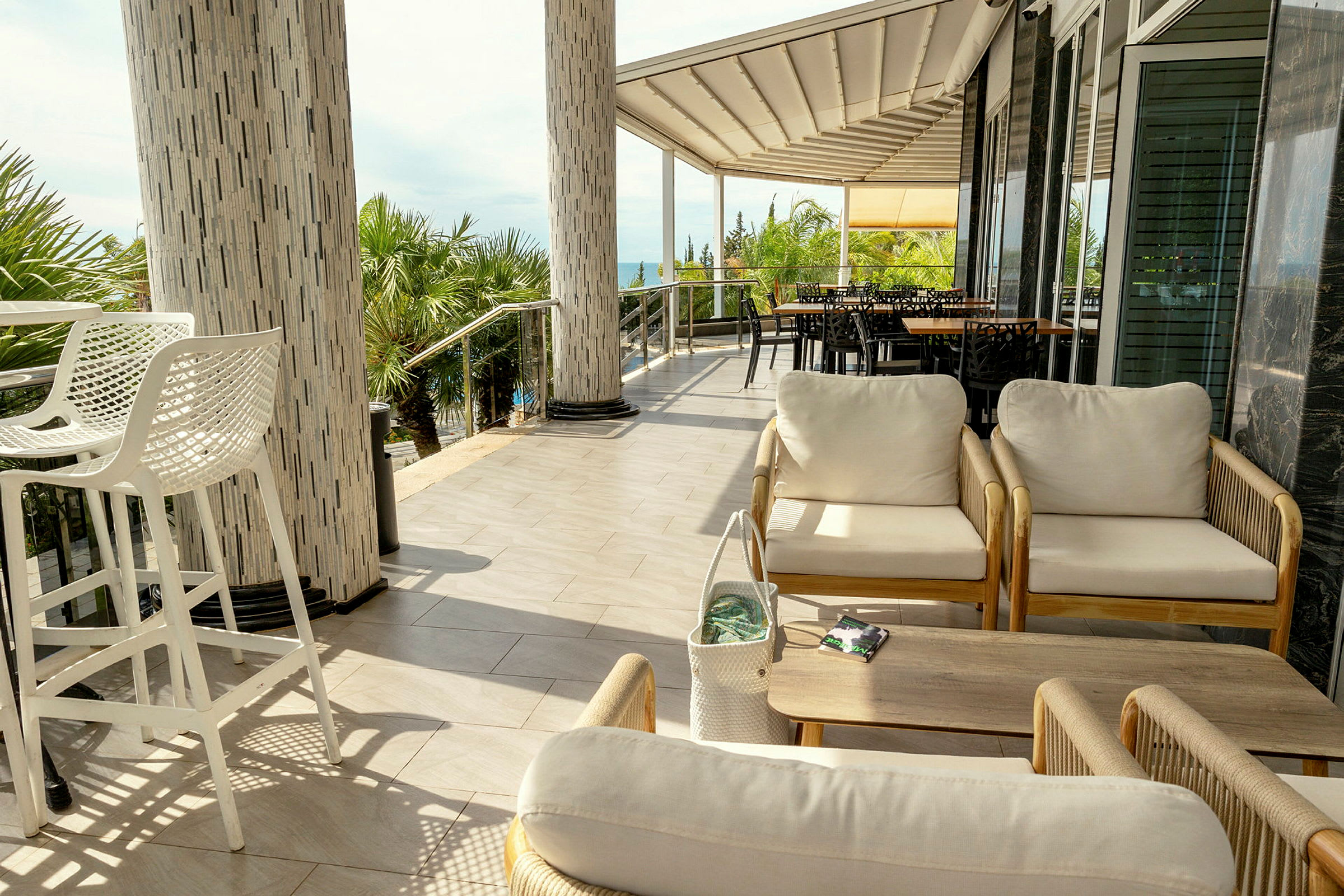 En terrasse med sittemøbler, palmeskog og havet i bakgrunnen. (AI-generert tekst)