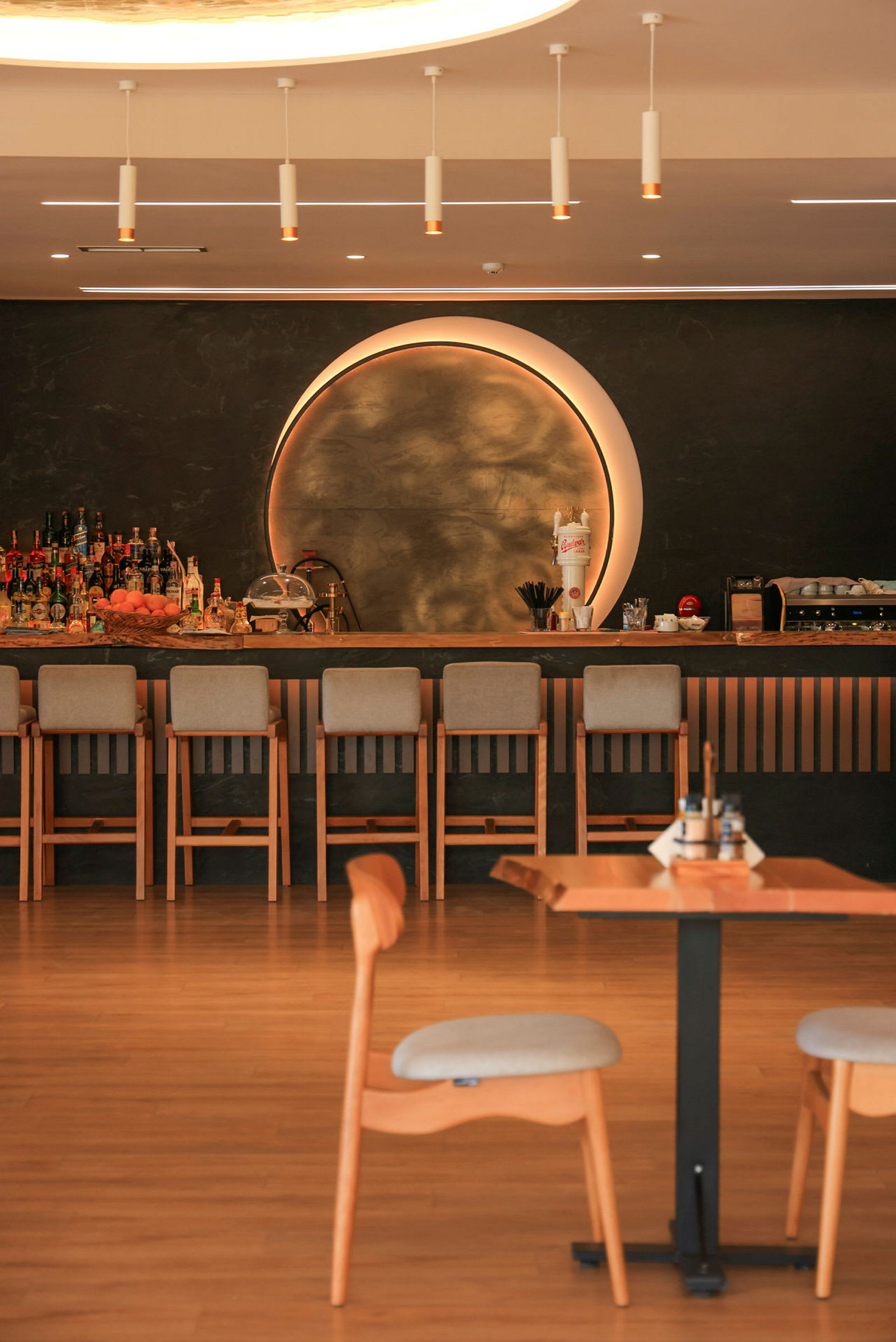 Interiør av en bar med trebord og et belyst rundt dekorativt element på veggen. (AI-generert tekst)