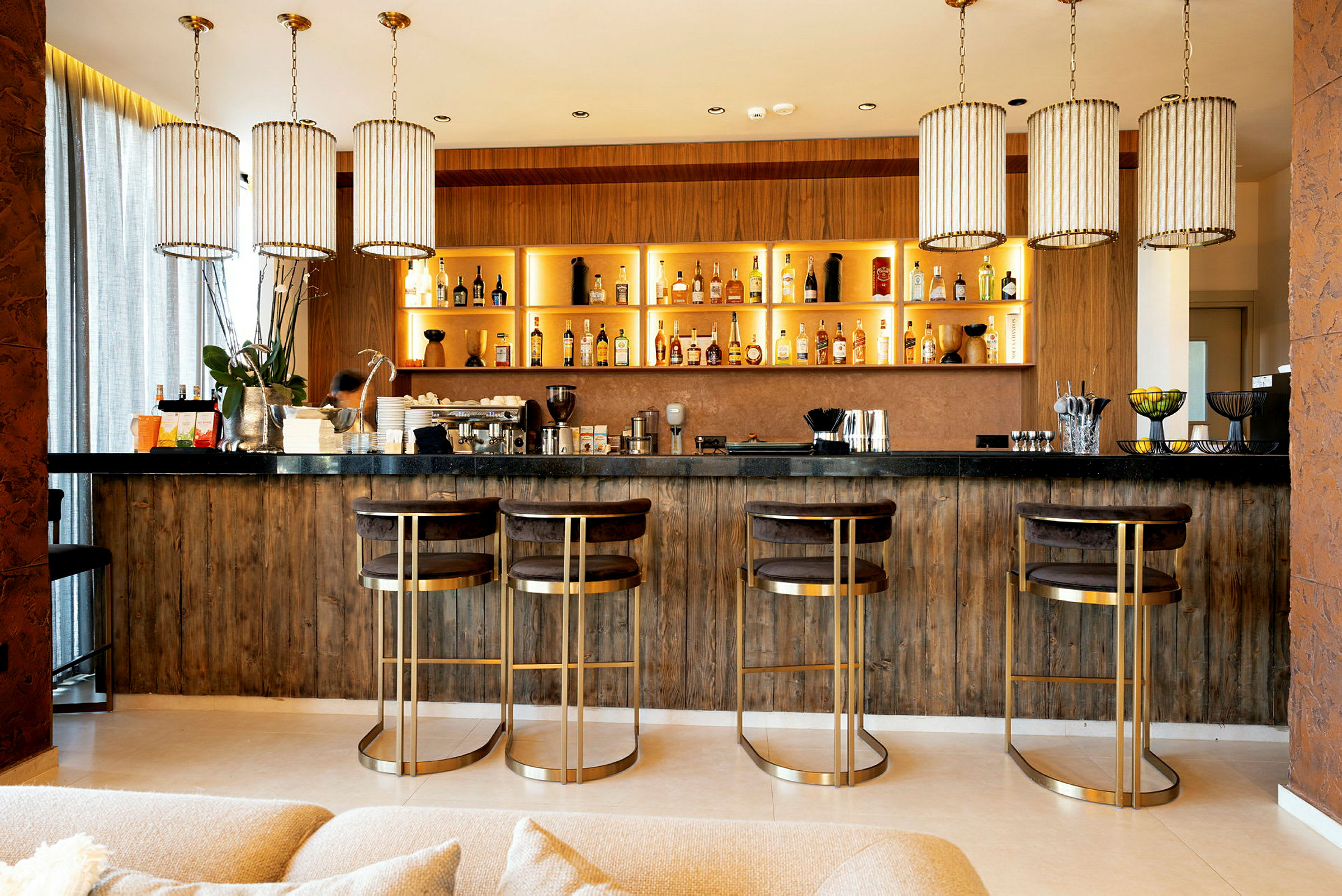 En elegant bar med fire høy stoler og hyller fulle av flasker. (AI-generert tekst)