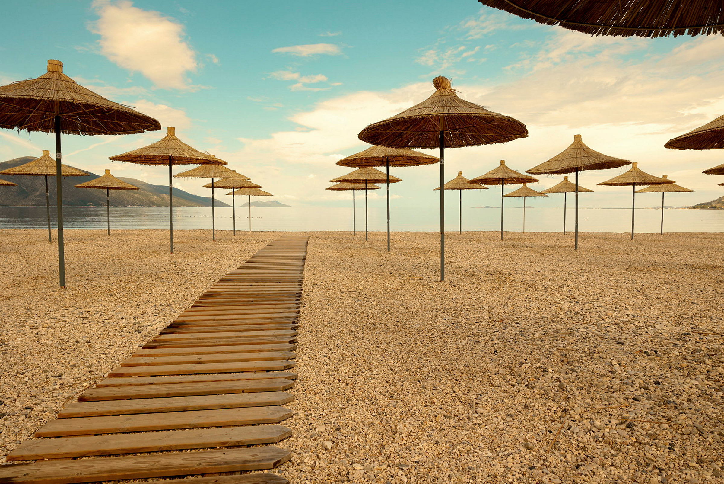 Strand med parasoller og tresti som leder mot havet. (AI-generert tekst)