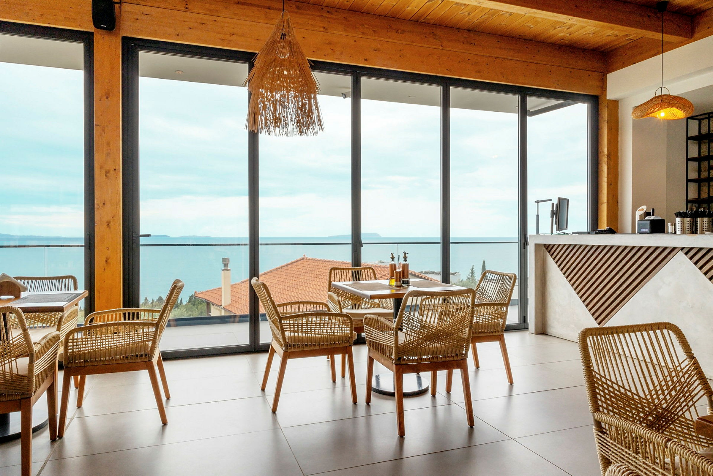 En restaurant med rottingmøbler og store vinduer som vender ut mot havet. (AI-generert tekst)