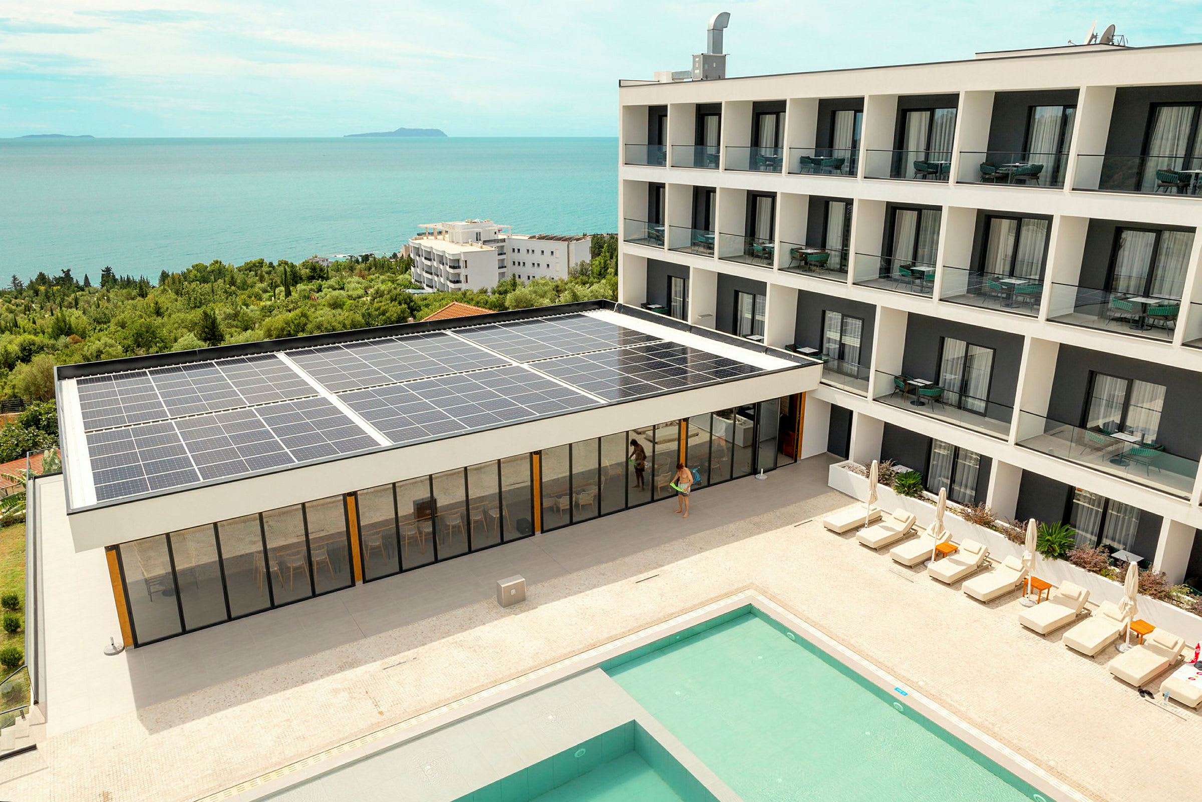 Hotellbygning med solcellepaneler, basseng og solsenger, i nærheten av kysten. (AI-generert tekst)