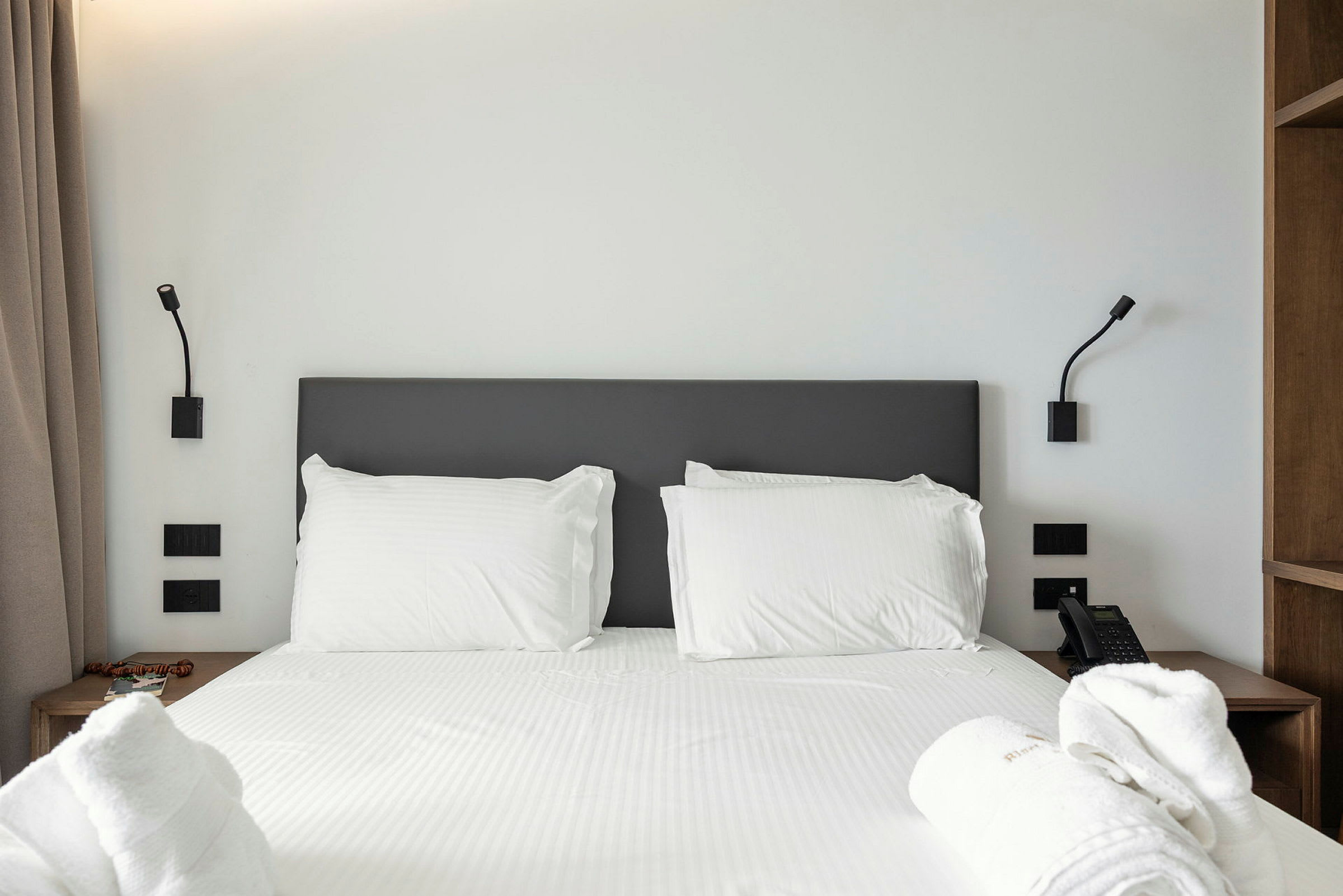 En hotellseng med hvite laken og puter, flankert av to nattlamper. (AI-generert tekst)