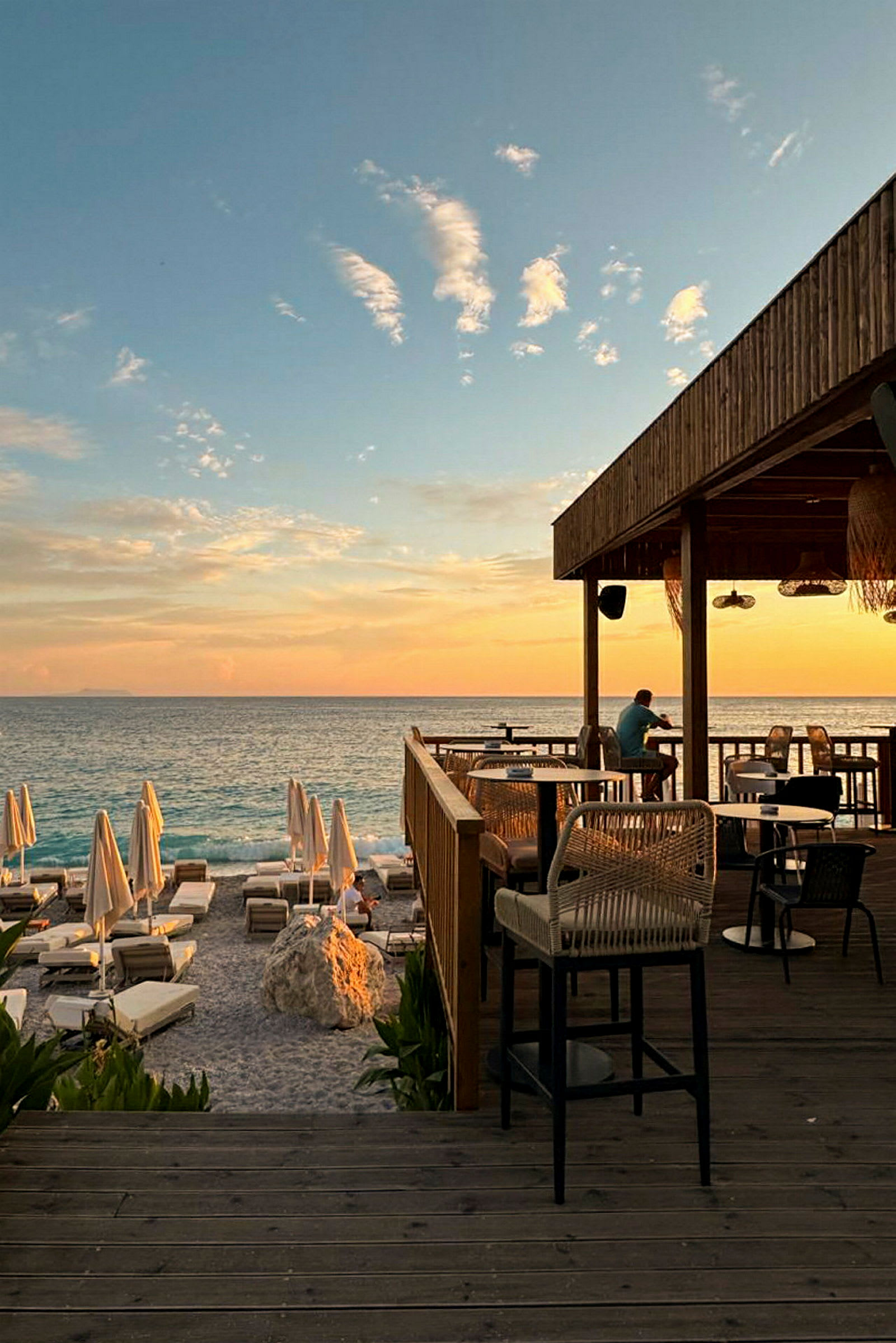 En solnedgang ved havet med en restaurantterrasse og solsenger på stranden. (AI-generert tekst)