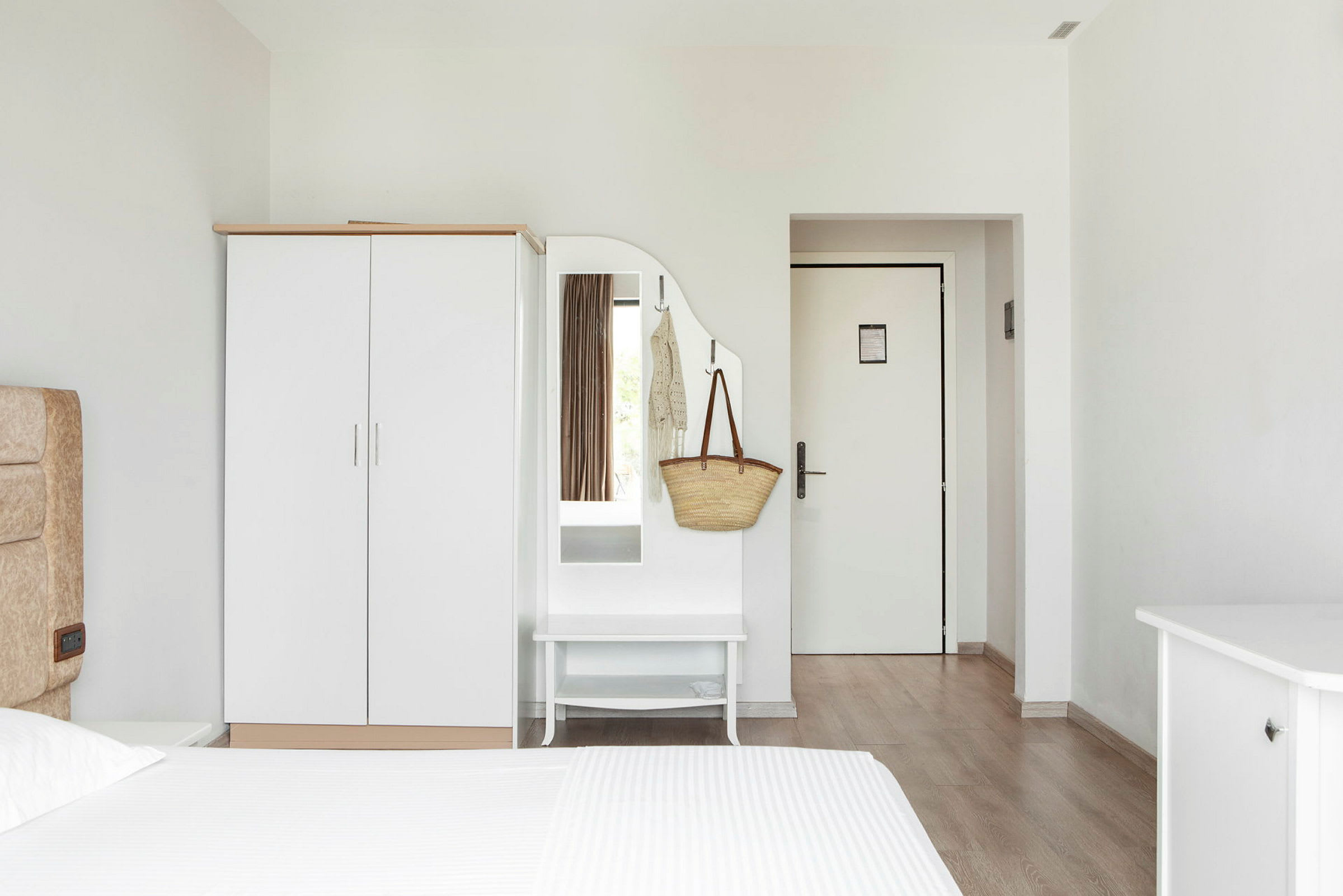Et hotellrom med en hvit garderobe, speil og dør. (AI-generert tekst)