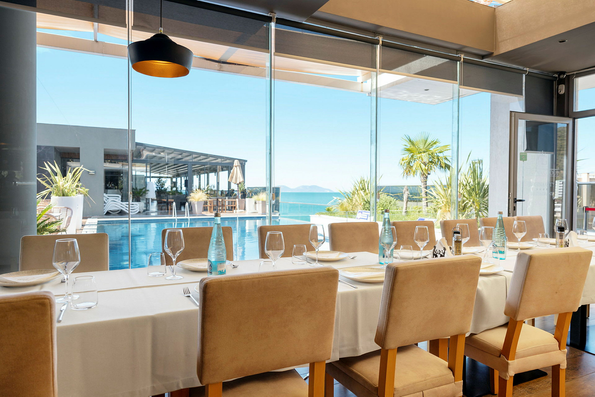 Restaurant med dekket bord og utsikt mot basseng og hav. (AI-generert tekst)
